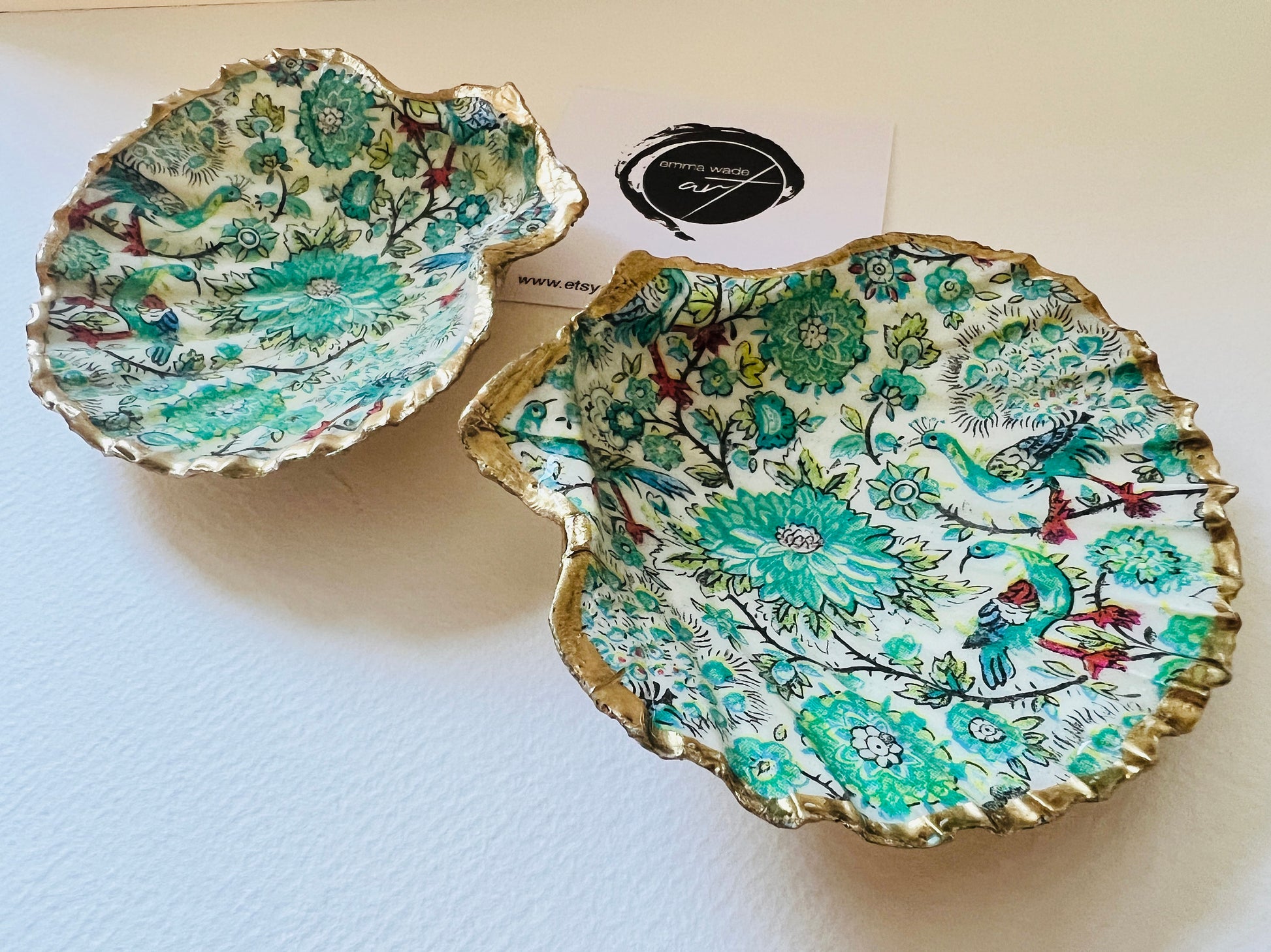 Handmade Dorset scallop shell trinket dishes featuring intricate green peacock inspired artwork in emerald, turquoise and gold tones with hand-painted gold leaf edging and glossy crystal clear resin. Elegant coastal jewellery dishes styled on a neutral background with nature inspired bird motifs and luxurious gilded detailing.