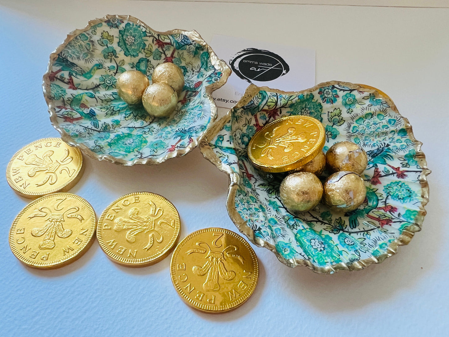 Handmade Dorset scallop shell trinket dishes featuring intricate green peacock inspired artwork in emerald, turquoise and gold tones with hand-painted gold leaf edging and glossy crystal clear resin. Elegant coastal jewellery dishes styled on a neutral background with nature inspired bird motifs and luxurious gilded detailing.