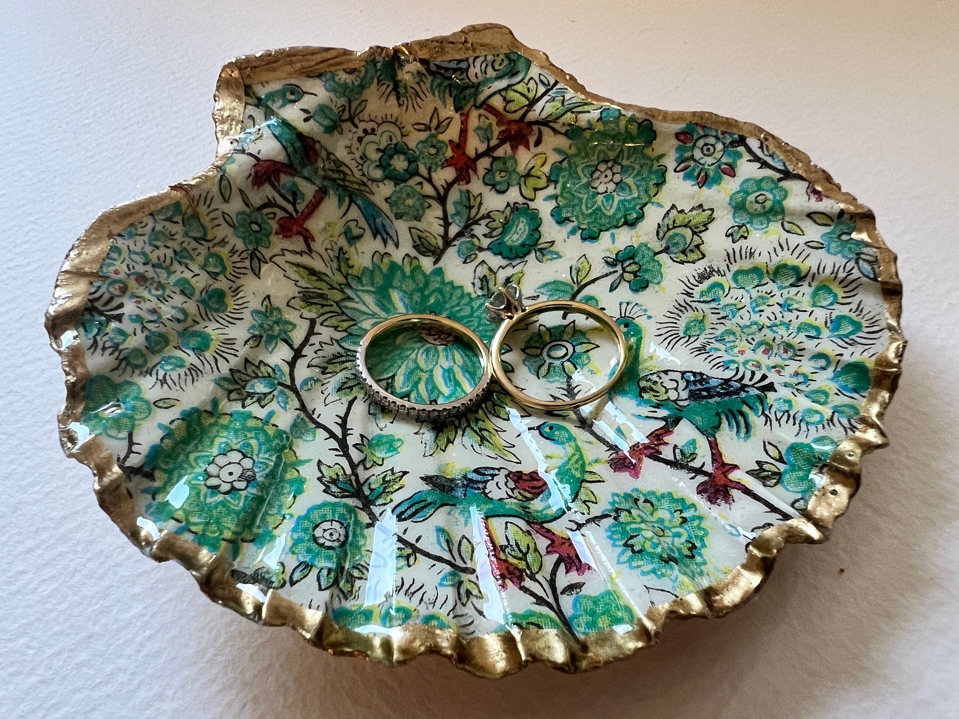 Handmade Dorset scallop shell trinket dishes featuring intricate green peacock inspired artwork in emerald, turquoise and gold tones with hand-painted gold leaf edging and glossy crystal clear resin. Elegant coastal jewellery dishes styled on a neutral background with nature inspired bird motifs and luxurious gilded detailing.