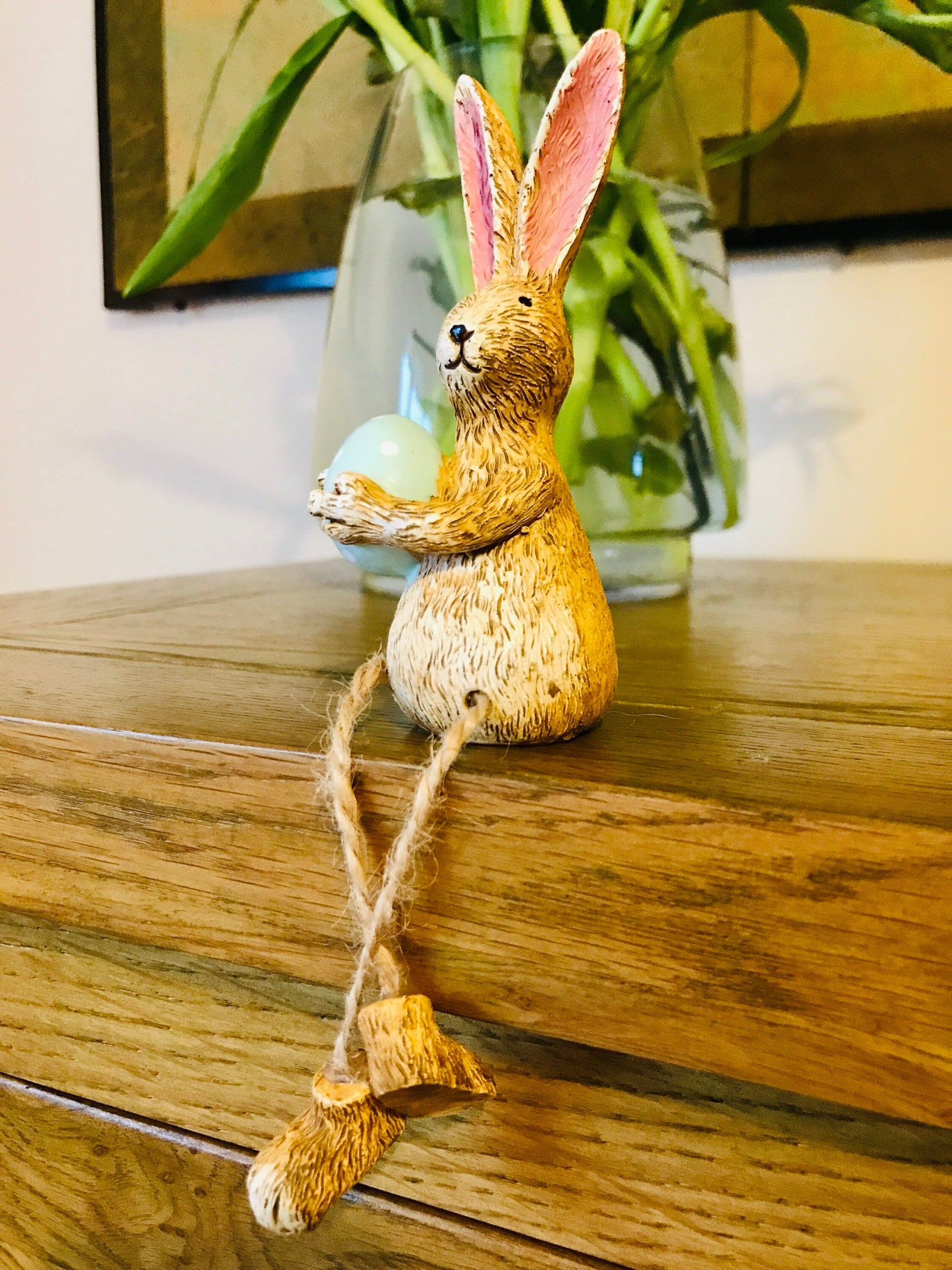 Hand-finished shelf sitting bunny ornament with dangling jute legs and polka dot egg. Available in pink or green. Perfect Easter rabbit shelf decoration, birthday gift, or home décor accessory. Cute animal figurine for rabbit lovers, Easter decorations, new home presents, or seasonal mantel styling.