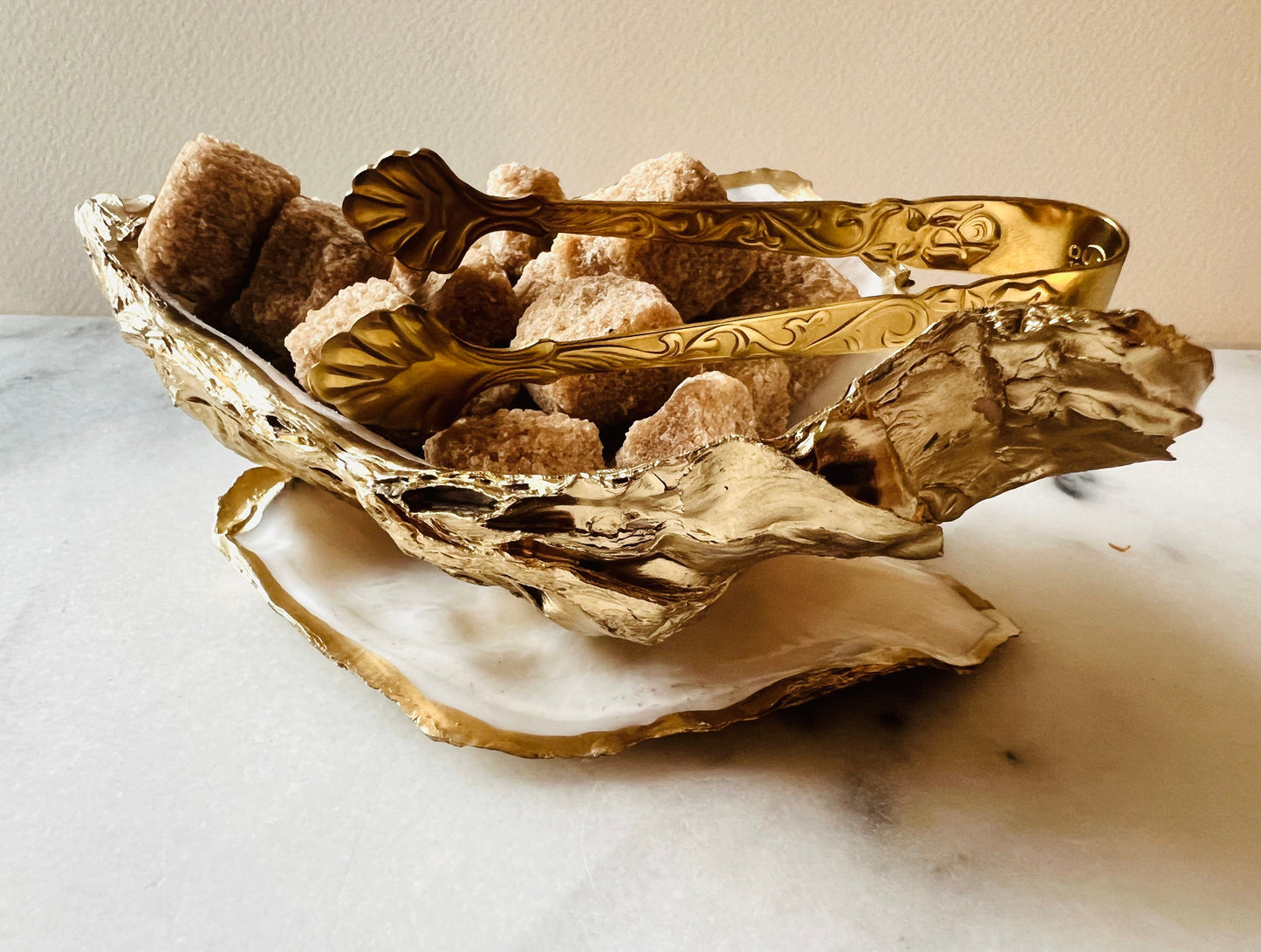 Extra large Dorset oyster shell serving dish set with natural pearl interior and hand-applied gold leaf edging, featuring a cupped XL oyster shell with matching flat shell base. Luxury coastal home décor ideal as a sugar dish, serving bowl, coffee station accessory, or elegant host gift. Handmade using sustainably sourced UK oyster shells and finished with glossy resin and optional gold serving accessories.