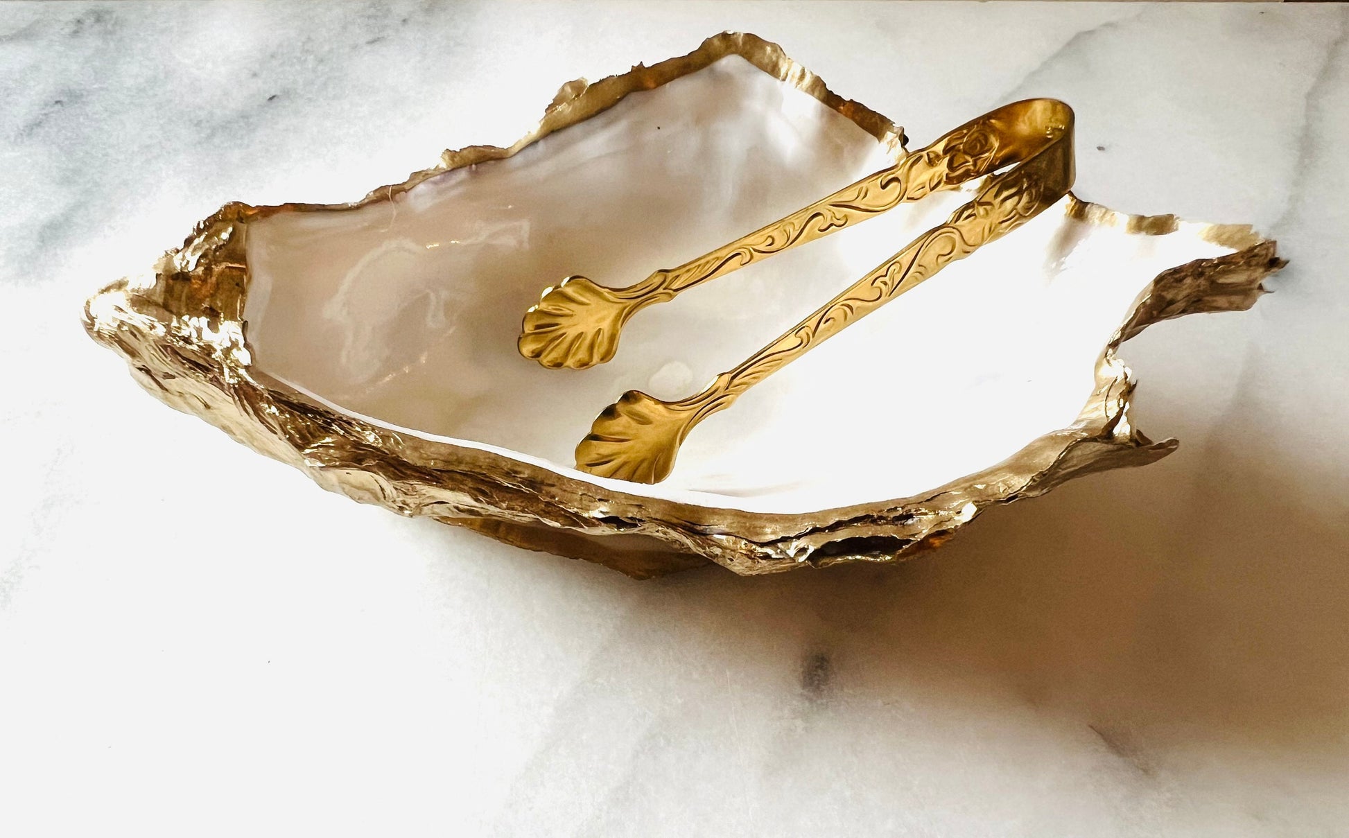 Extra large Dorset oyster shell serving dish set with natural pearl interior and hand-applied gold leaf edging, featuring a cupped XL oyster shell with matching flat shell base. Luxury coastal home décor ideal as a sugar dish, serving bowl, coffee station accessory, or elegant host gift. Handmade using sustainably sourced UK oyster shells and finished with glossy resin and optional gold serving accessories.