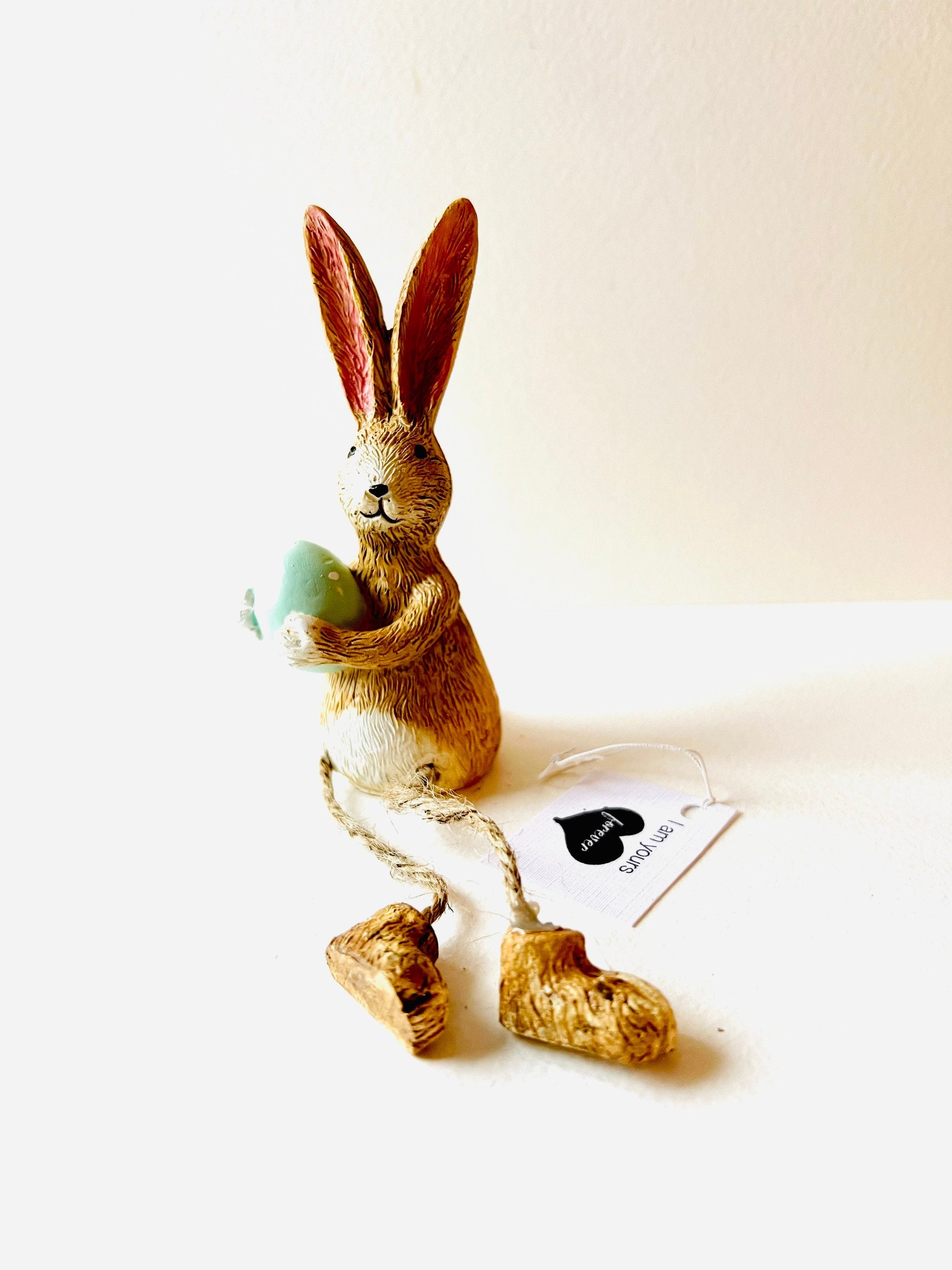 Hand-finished shelf sitting bunny ornament with dangling jute legs and polka dot egg. Available in pink or green. Perfect Easter rabbit shelf decoration, birthday gift, or home décor accessory. Cute animal figurine for rabbit lovers, Easter decorations, new home presents, or seasonal mantel styling.