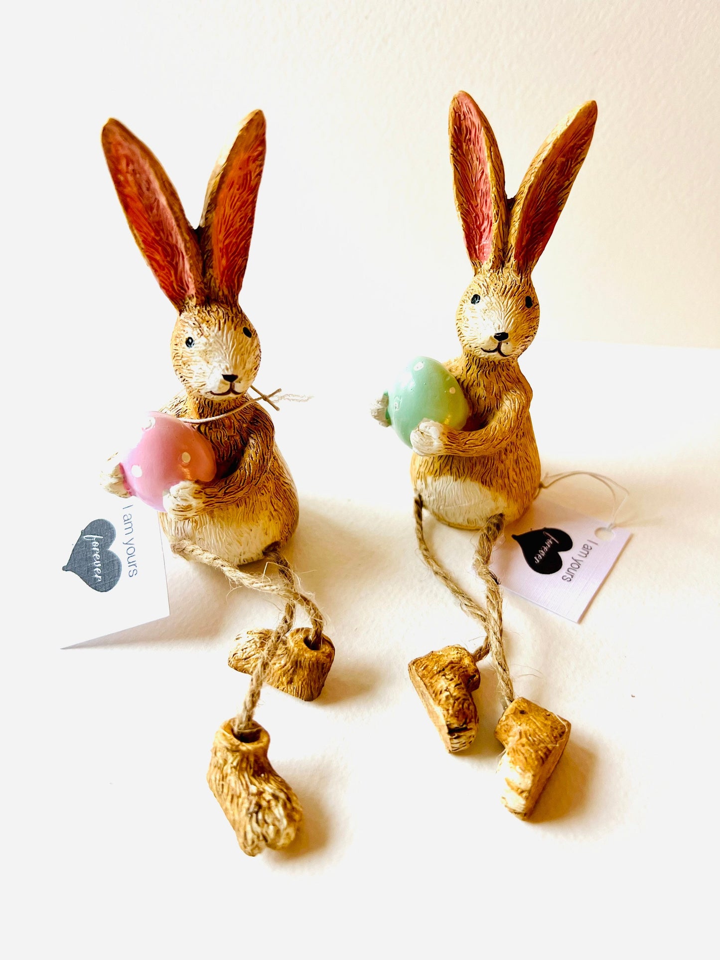 Hand-finished shelf sitting bunny ornament with dangling jute legs and polka dot egg. Available in pink or green. Perfect Easter rabbit shelf decoration, birthday gift, or home décor accessory. Cute animal figurine for rabbit lovers, Easter decorations, new home presents, or seasonal mantel styling.