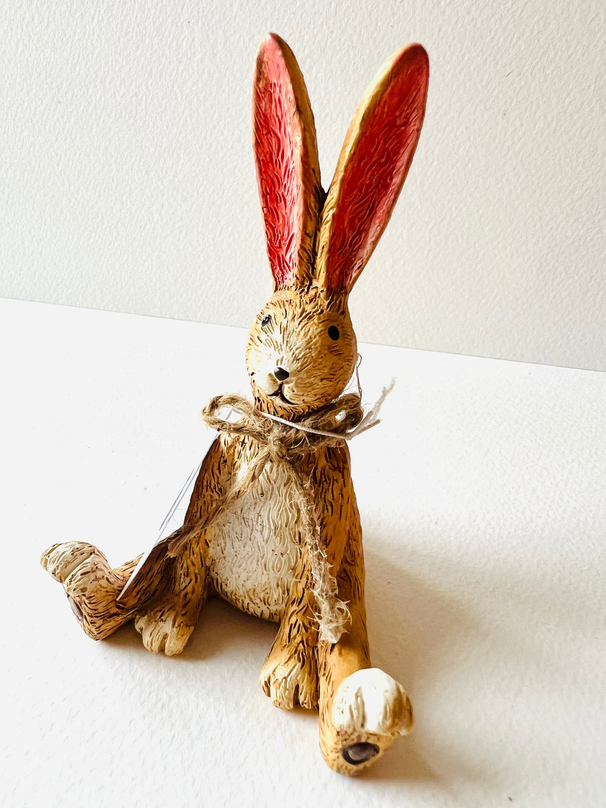 Hand finished polyresin Christmas bunny ornaments with rustic jute bows and soft pink inner ears. Decorative rabbit shelf ornaments shown as a seated bunny and two bunnies kissing, available individually or as a set. Festive woodland-style decor for Christmas shelves, mantelpieces, cottage interiors and rabbit lover gifts.