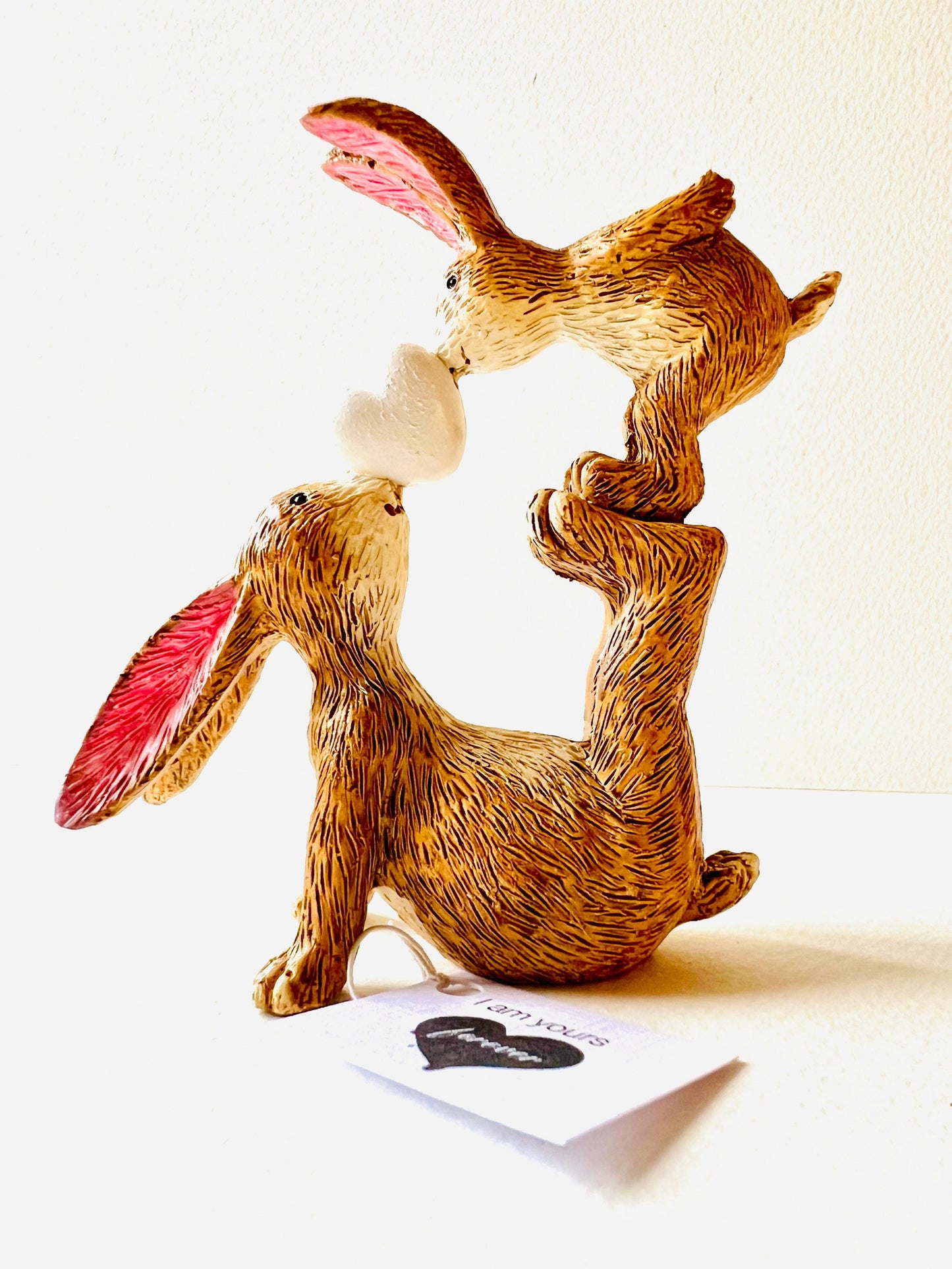 Hand finished polyresin bunny ornament showing mother rabbit balancing baby bunny on her feet while holding a small heart, rustic brown textured finish with pink inner ears.