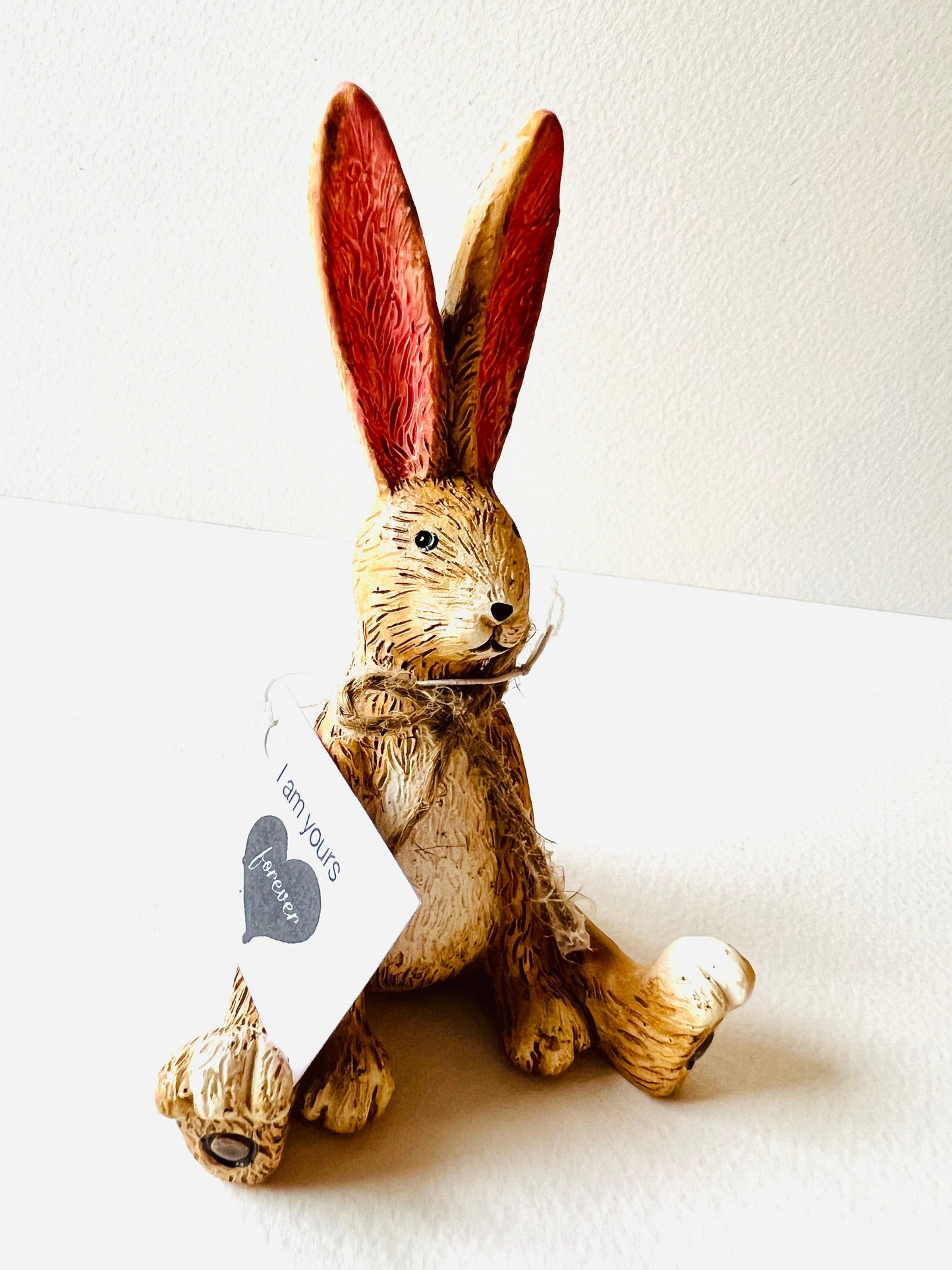 Hand finished polyresin sitting bunny ornament with upright pink ears and rustic jute bow, textured brown rabbit figurine displayed on wooden stand.