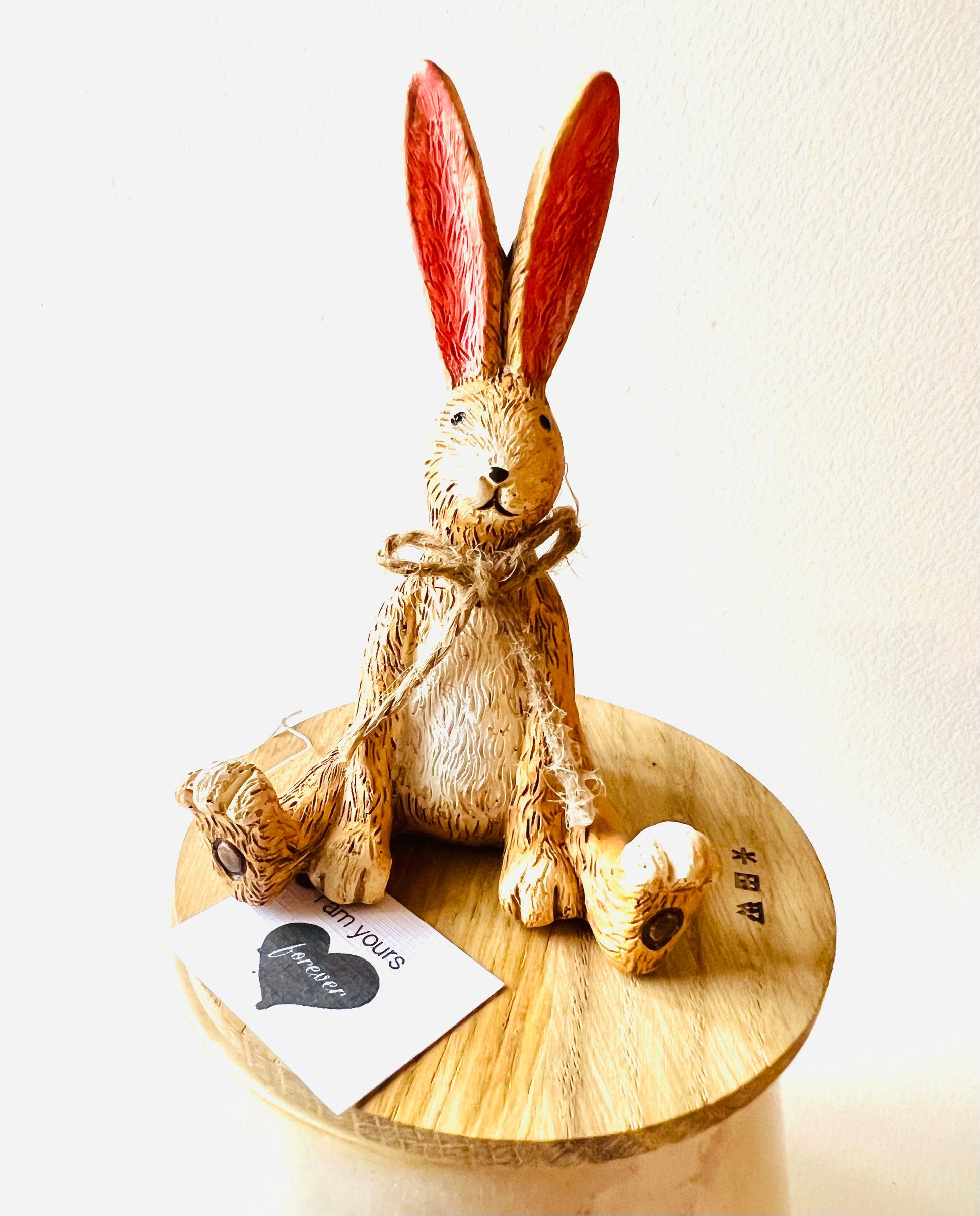 Hand finished polyresin sitting bunny ornament with upright pink ears and rustic jute bow, textured brown rabbit figurine displayed on wooden stand.