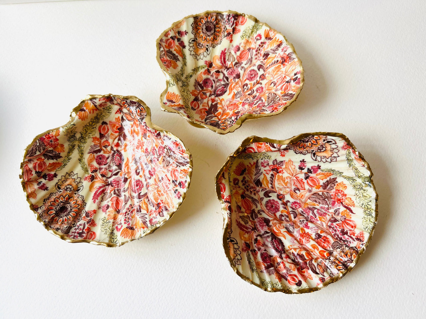 Handmade Dorset scallop shell trinket dish featuring a William Morris inspired pink floral botanical design in coral, berry and soft gold tones. Decorative jewellery holder finished with hand-applied liquid gold leaf edging and glossy resin. Heritage style coastal décor shell dish with romantic English country house aesthetic, styled as a ring holder and elegant vanity accessory.