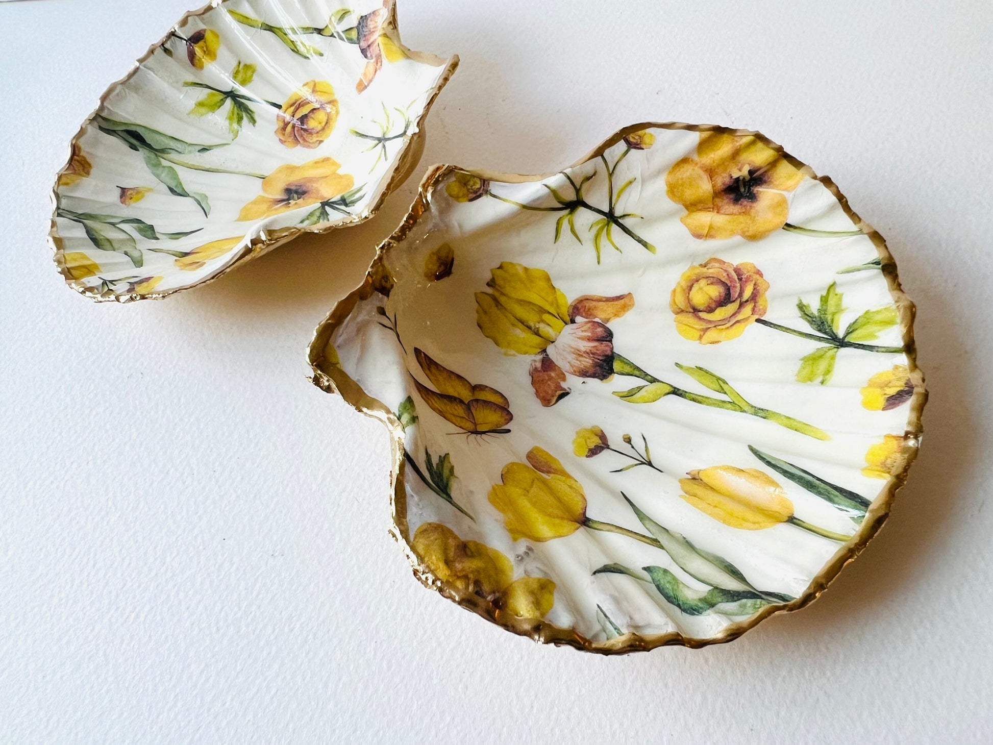 Hand finished scallop shell trinket dish featuring yellow spring flower artwork with a hand gilded gold leaf rim, sealed in glossy clear resin for durability and shine. Coastal inspired shell jewellery dish photographed on a light surface, ideal for rings, earrings and small keepsakes. Decorative floral shell dish by EmmaWadeART inspired by the Dorset coastline, perfect as a gift or elegant home décor accent.