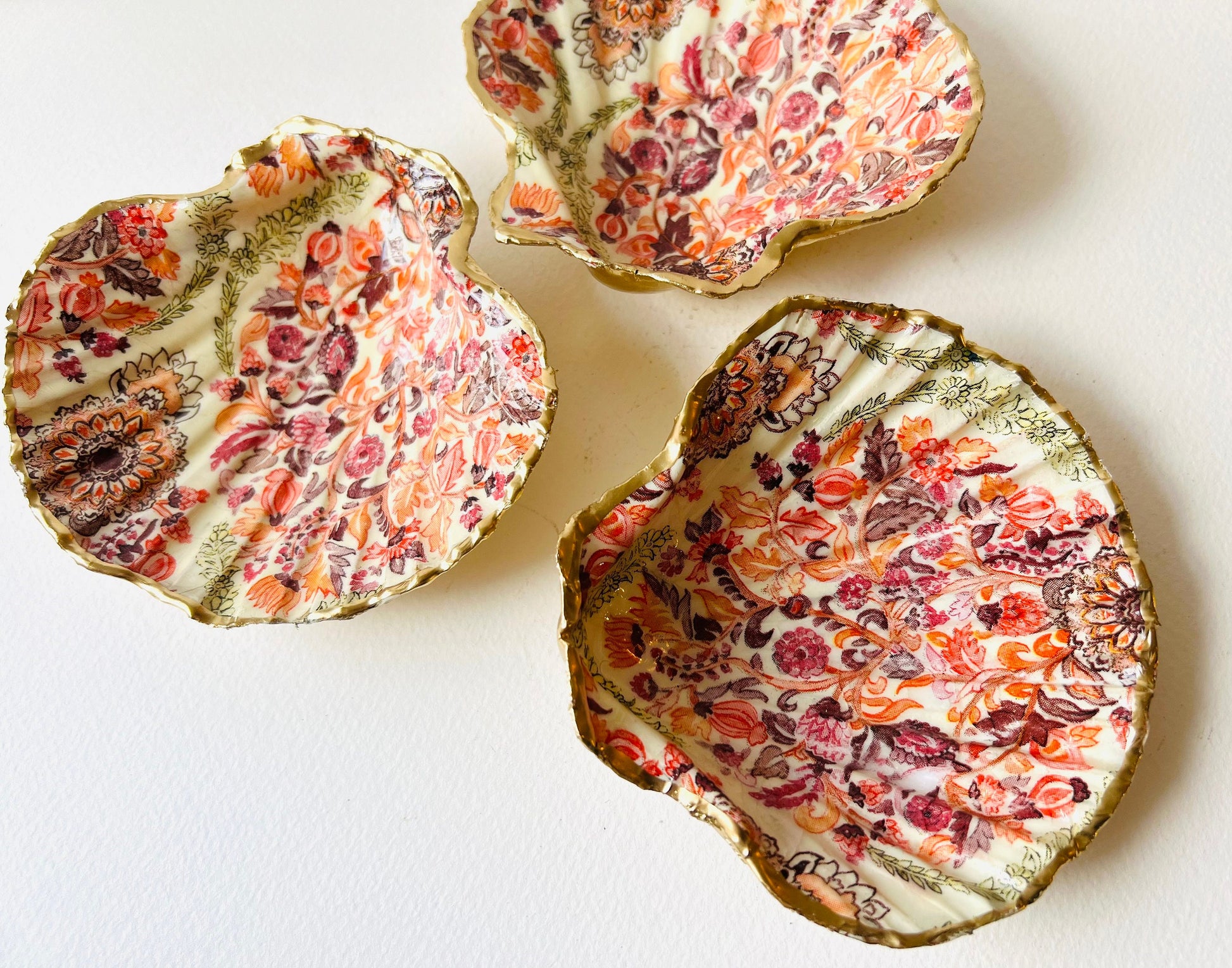 Handmade Dorset scallop shell trinket dish featuring a William Morris inspired pink floral botanical design in coral, berry and soft gold tones. Decorative jewellery holder finished with hand-applied liquid gold leaf edging and glossy resin. Heritage style coastal décor shell dish with romantic English country house aesthetic, styled as a ring holder and elegant vanity accessory.