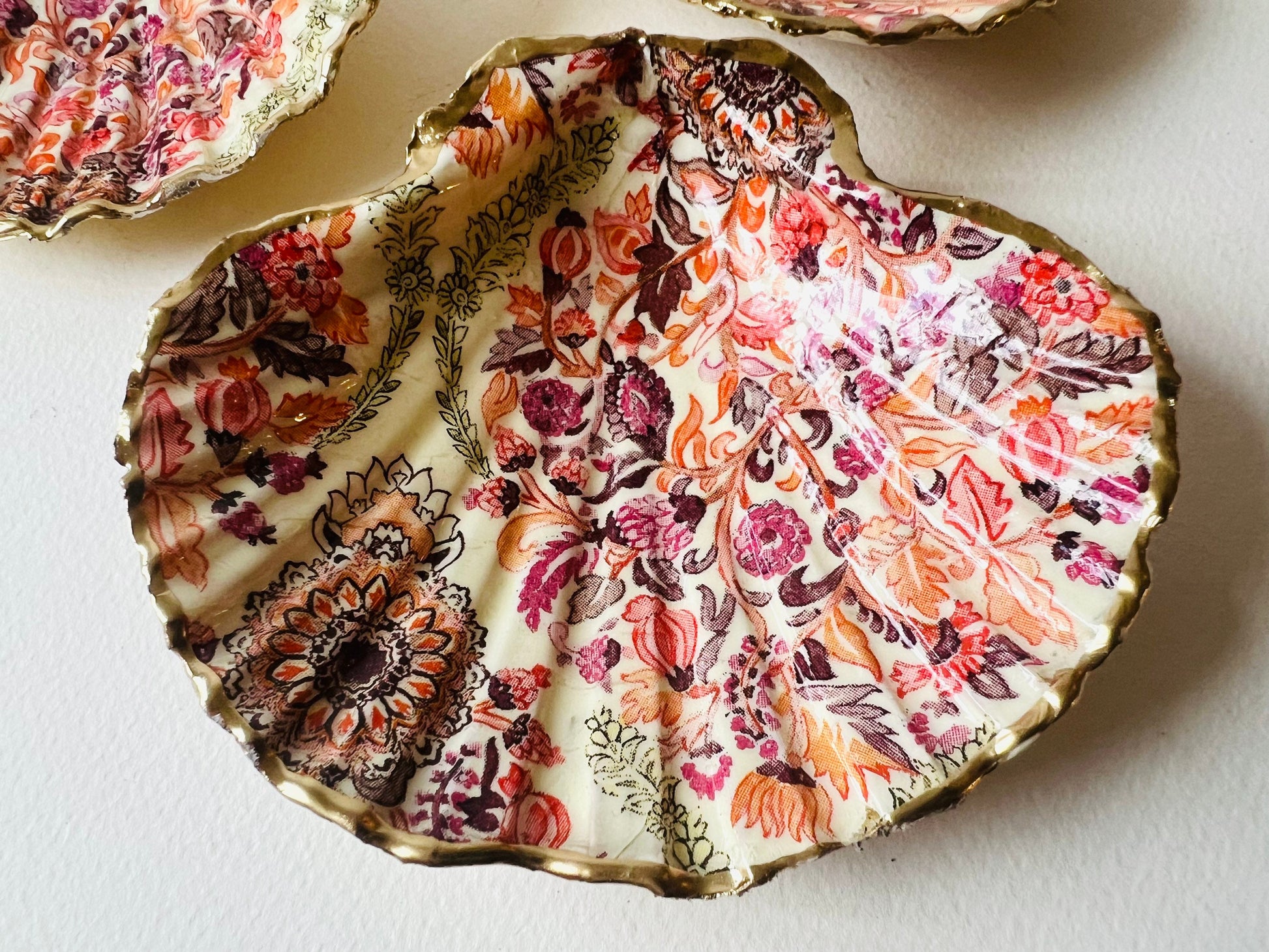 Handmade Dorset scallop shell trinket dish featuring a William Morris inspired pink floral botanical design in coral, berry and soft gold tones. Decorative jewellery holder finished with hand-applied liquid gold leaf edging and glossy resin. Heritage style coastal décor shell dish with romantic English country house aesthetic, styled as a ring holder and elegant vanity accessory.