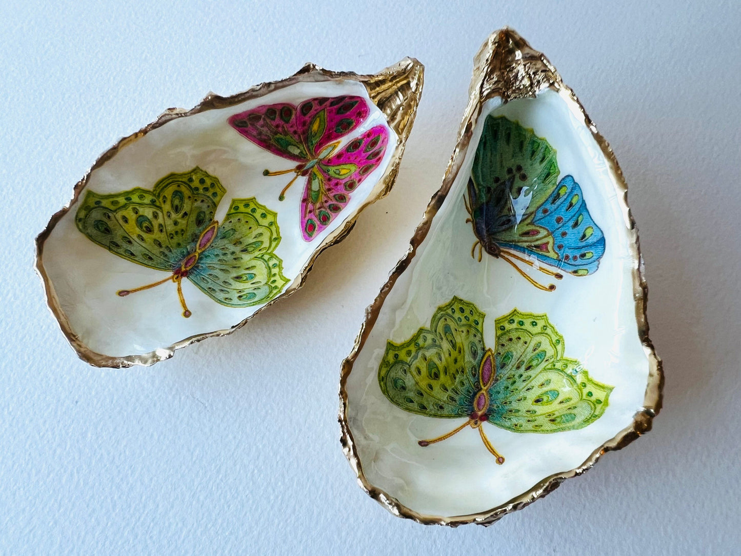Handmade butterfly oyster shell trinket dish with colourful blue green and pink butterfly designs, edged and backed in gold leaf, Dorset coastal shell jewellery holder with glossy resin finish, luxury ring dish, coastal home decor gift, unique handmade shell dish for jewellery storage, beach house accessory, UK artisan oyster shell dish