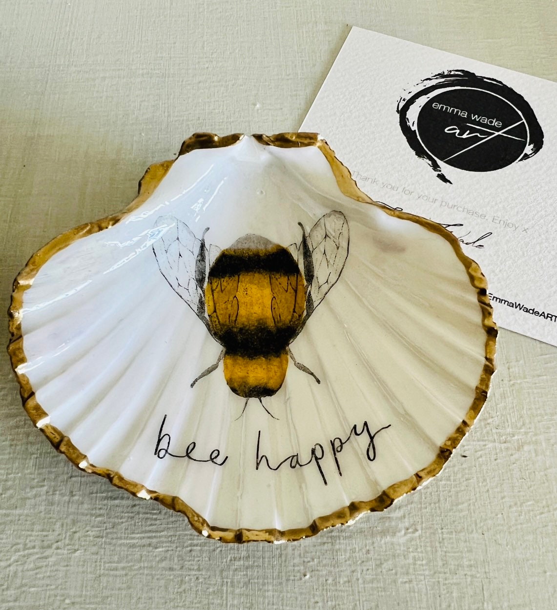 Handmade scallop shell trinket dish featuring a bumblebee illustration with gold leaf edging and glossy resin finish. Coastal jewellery dish in natural white shell with bee artwork, displayed as a ring holder and handmade bee lover gift