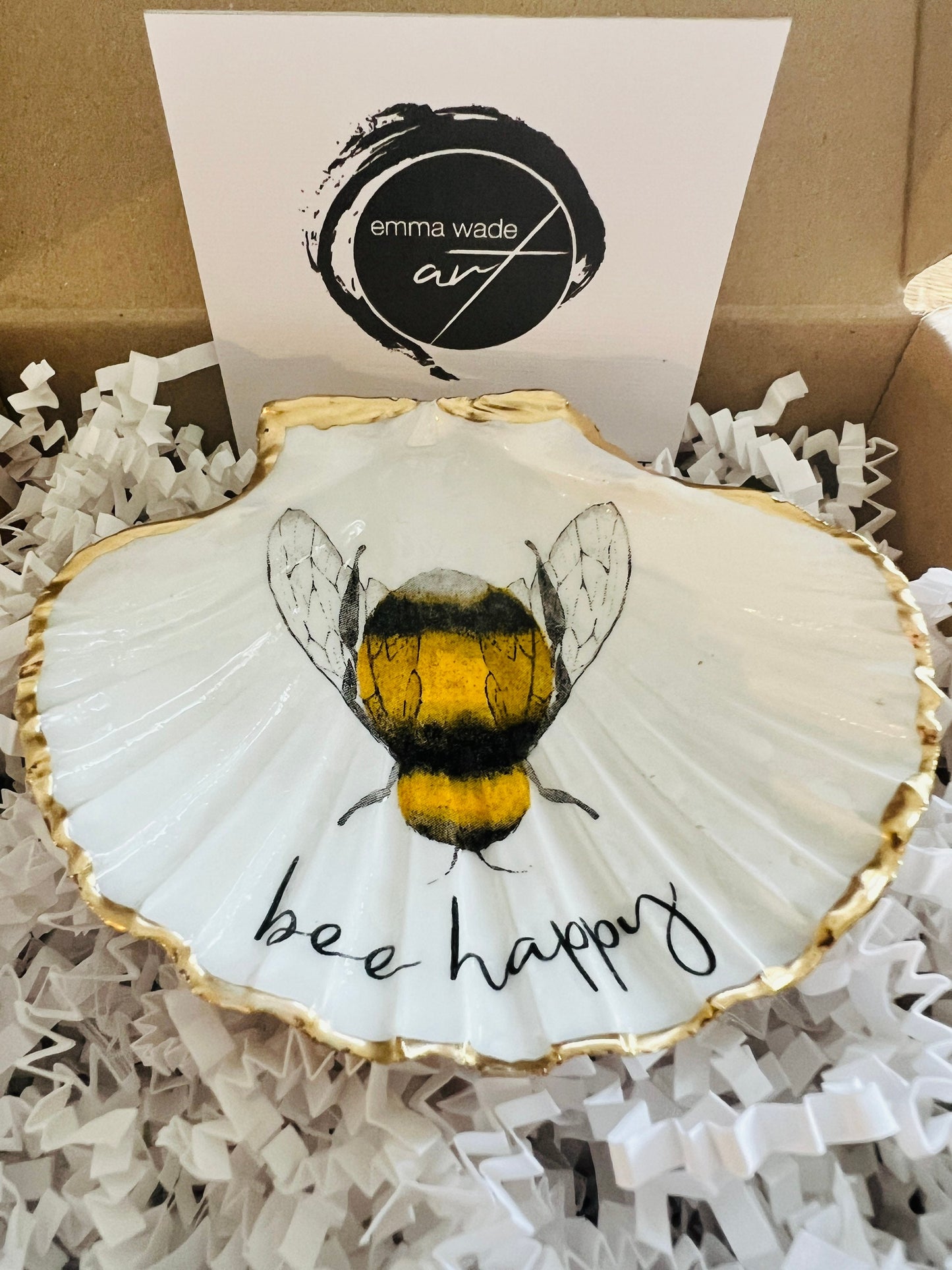 Handmade scallop shell trinket dish featuring a bumblebee illustration with gold leaf edging and glossy resin finish. Coastal jewellery dish in natural white shell with bee artwork, displayed as a ring holder and handmade bee lover gift