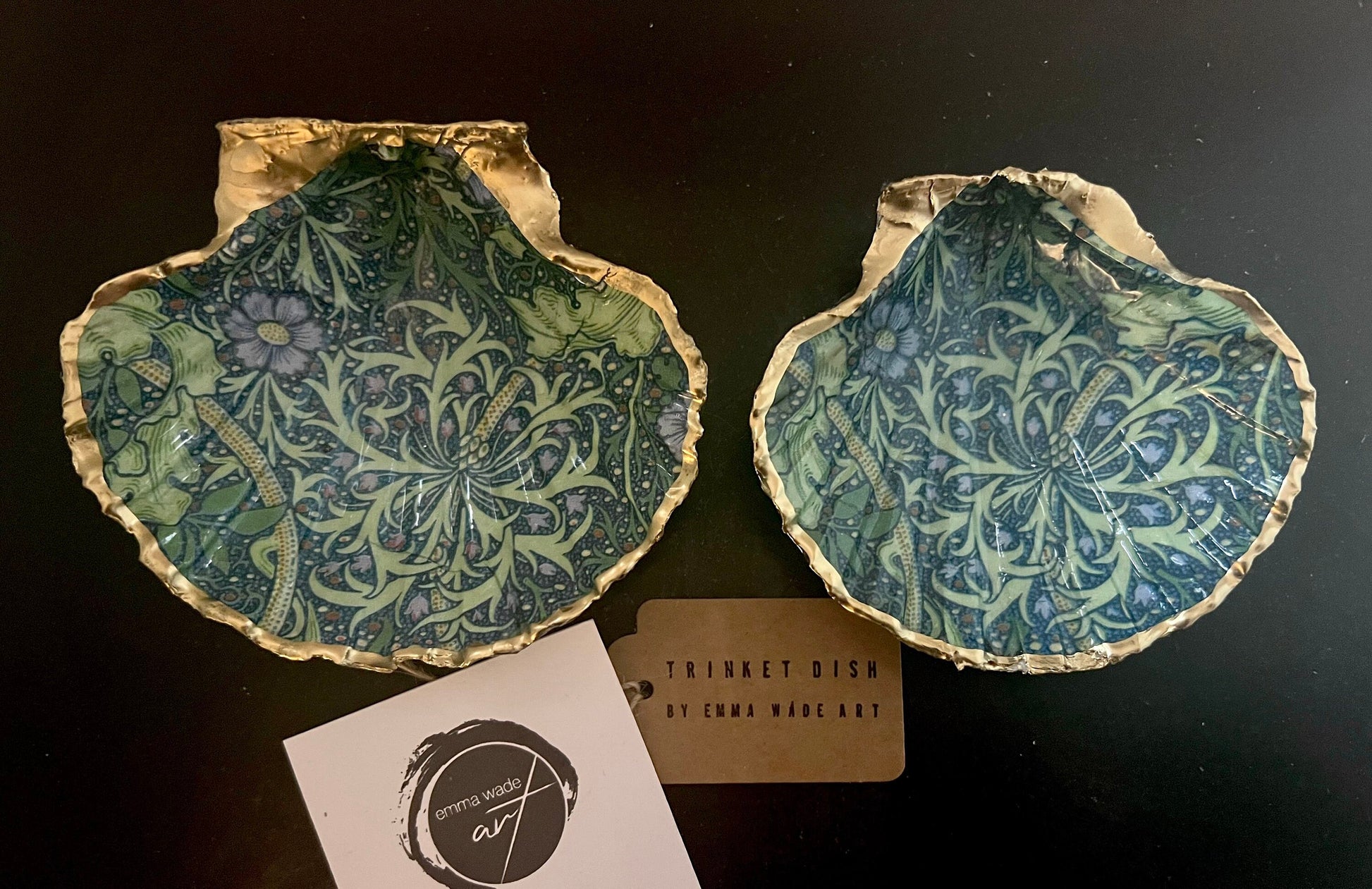 Handmade William Morris inspired scallop shell trinket dish in green and blue tones, featuring a seaweed decoupage design. Finished with gold leaf and sealed with glossy resin. Coastal jewellery dish made from a UK scallop shell, perfect for holding rings, earrings and small treasures. Decorative shell bowl photographed on a light background, showing the natural shell shape and gilded edges.