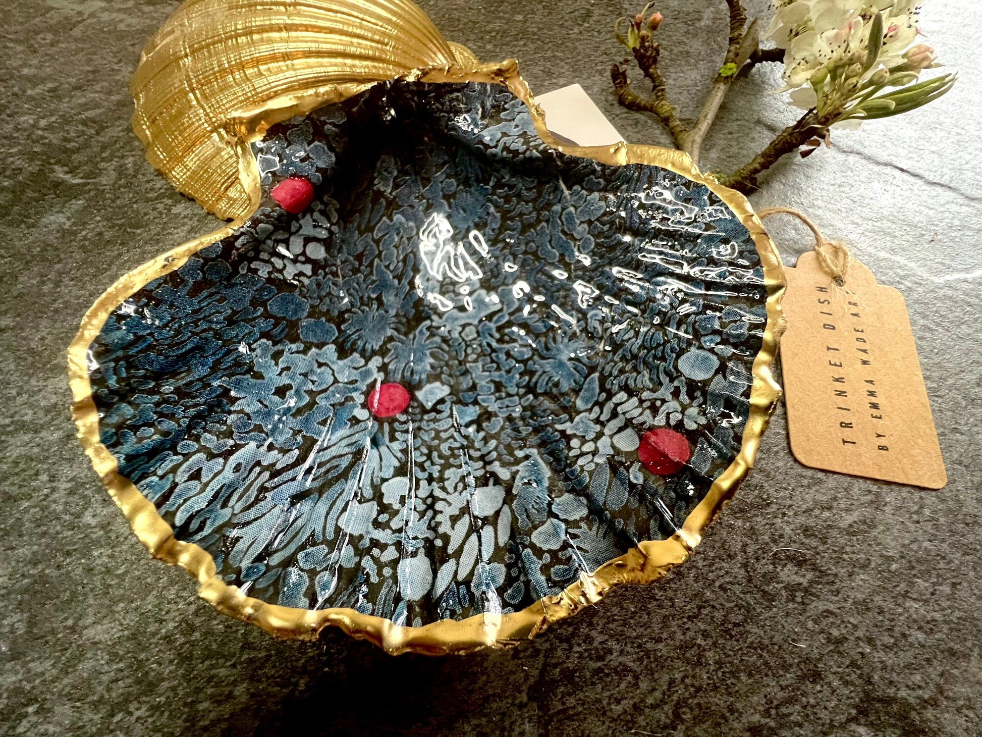 Handmade Marimekko inspired scallop shell trinket dish featuring bold Scandinavian floral design in deep blue with red accents. Natural Dorset scallop shell hand gilded with liquid gold leaf edging and sealed with glossy resin for a luxurious shine. Coastal home décor suitable as a jewellery dish, ring tray, trinket holder, wedding gift, bathroom décor or modern Nordic inspired shelf styling. Unique handcrafted shell décor inspired by botanical Scandinavian design.