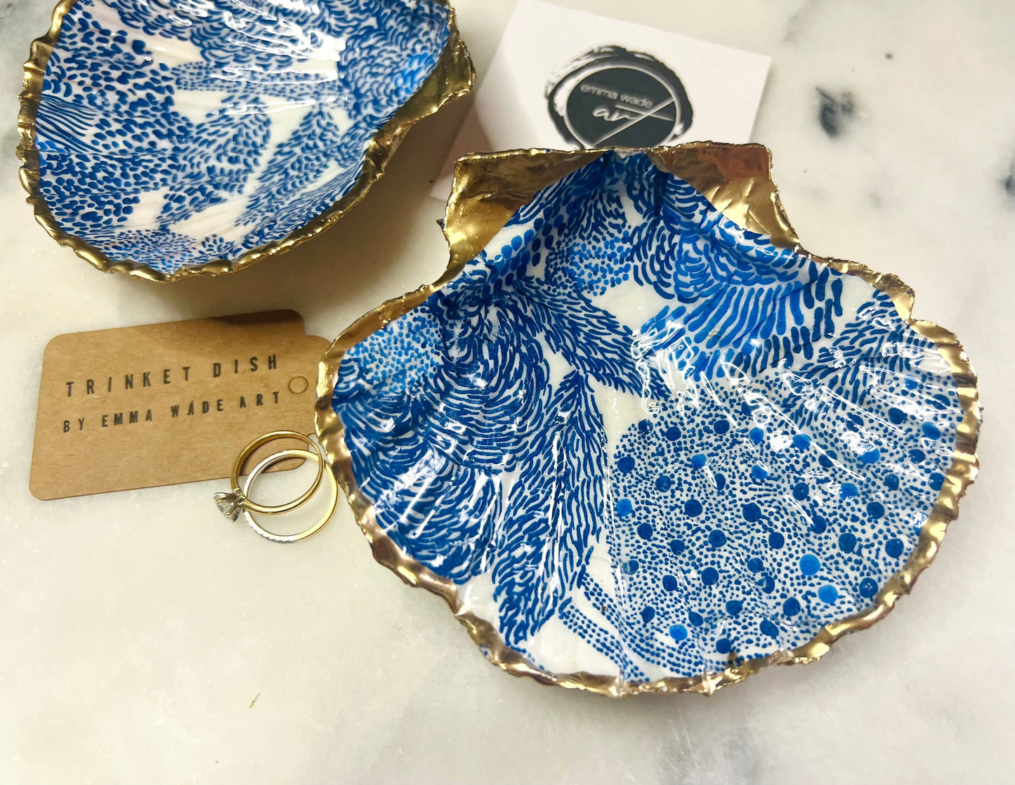 Marimekko inspired blue floral scallop shell trinket dish with hand-applied gold leaf edging and glossy resin finish. Natural Dorset shell jewellery holder featuring bold Scandinavian style botanical pattern. Decorative coastal ring dish styled on a marble surface, ideal as a bedside trinket bowl, host gift or luxury handmade home accent.