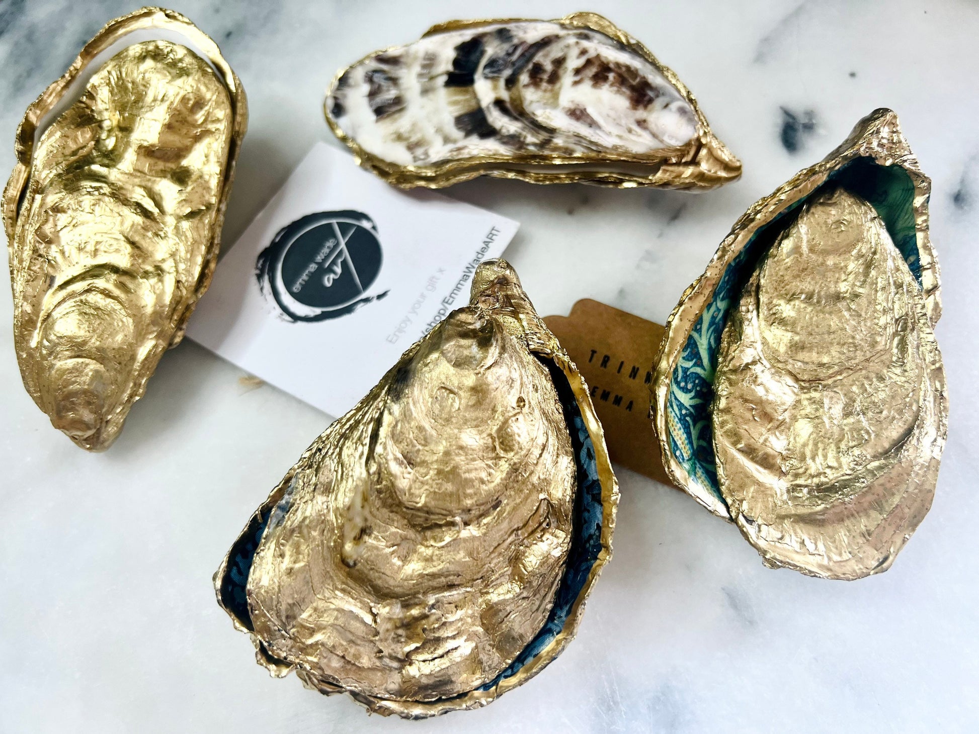 Selection of Dorset oyster shell ring and jewellery boxes in three designs, including natural pearl interior, gold leaf exterior, and patterned decoupage interior. Handcrafted oyster shells with matching lids, shown on a dark background with rings and packaging, highlighting the different finishes, gilded edges, and polished resin surfaces. Coastal keepsake boxes designed to hold engagement rings, wedding rings, or small jewellery items.