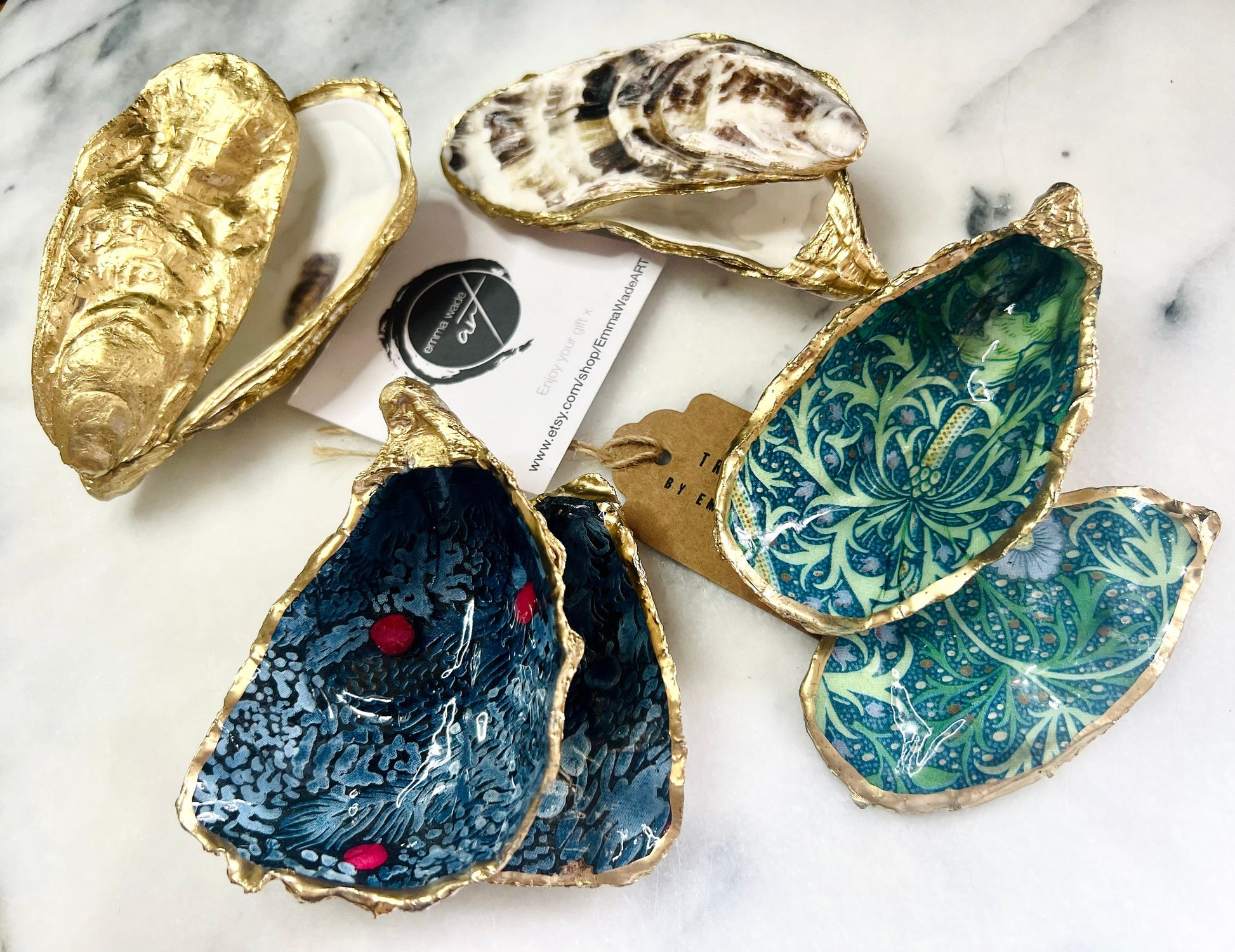 Luxury Dorset oyster shell ring and jewellery box with matching lid, finished with gold leaf detailing and glossy resin. 4 designs avaialble including natural oyster shell with gold rim and pearl interior, gold leaf shell with natural white interior, or gold leaf shell with decoupage interior. Shown holding rings on a light background, highlighting the natural shell shape and polished handcrafted coastal keepsake style. Ideal as an engagement ring box, wedding ring holder, or jewellery keepsake.