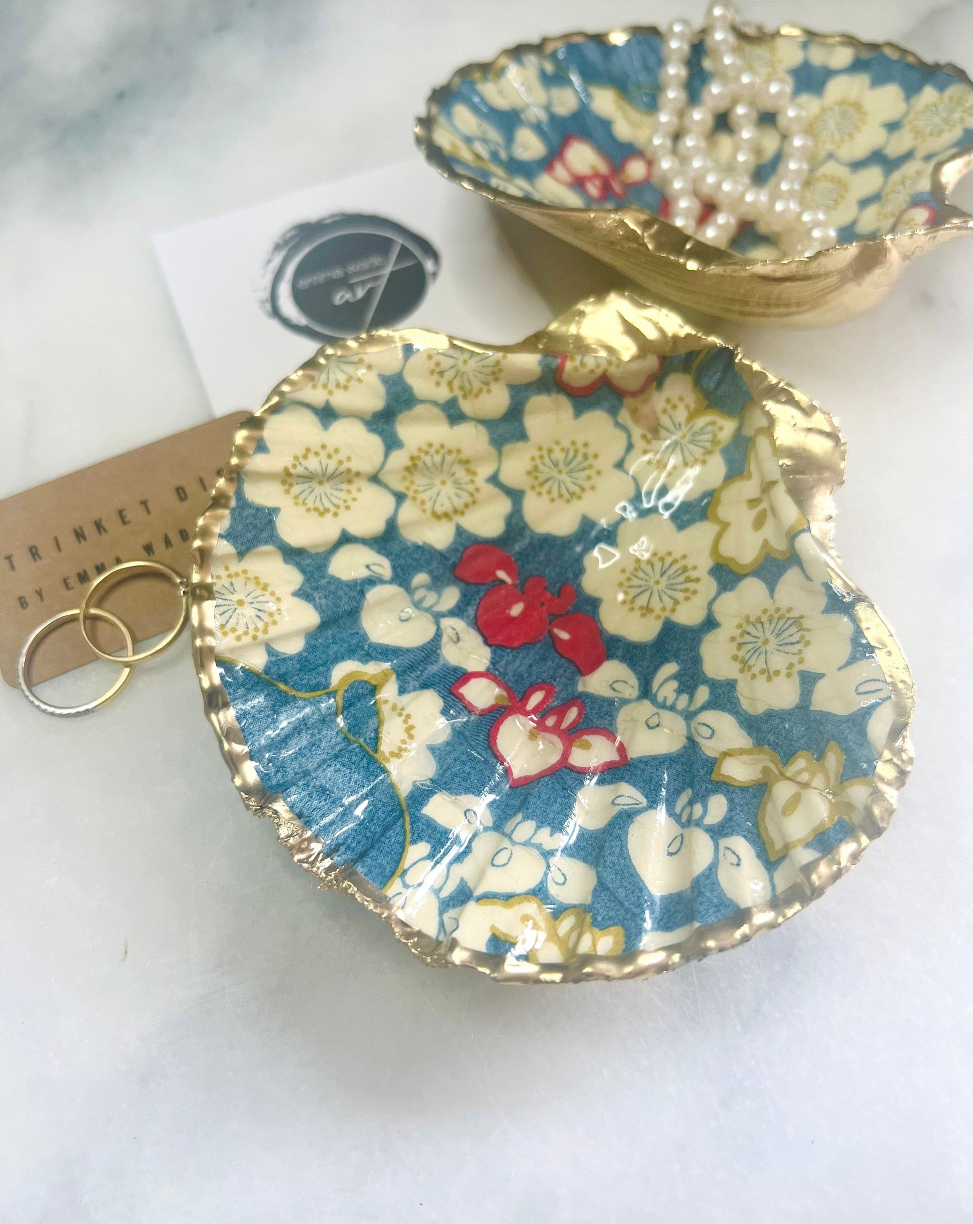 Japanese Sakura cherry blossom floral scallop shell trinket dish with blue, cream and red botanical flower design, hand finished with liquid gold leaf edging and glossy resin. Handmade coastal jewellery tray and ring dish inspired by Japanese floral art and Dorset coastal décor.