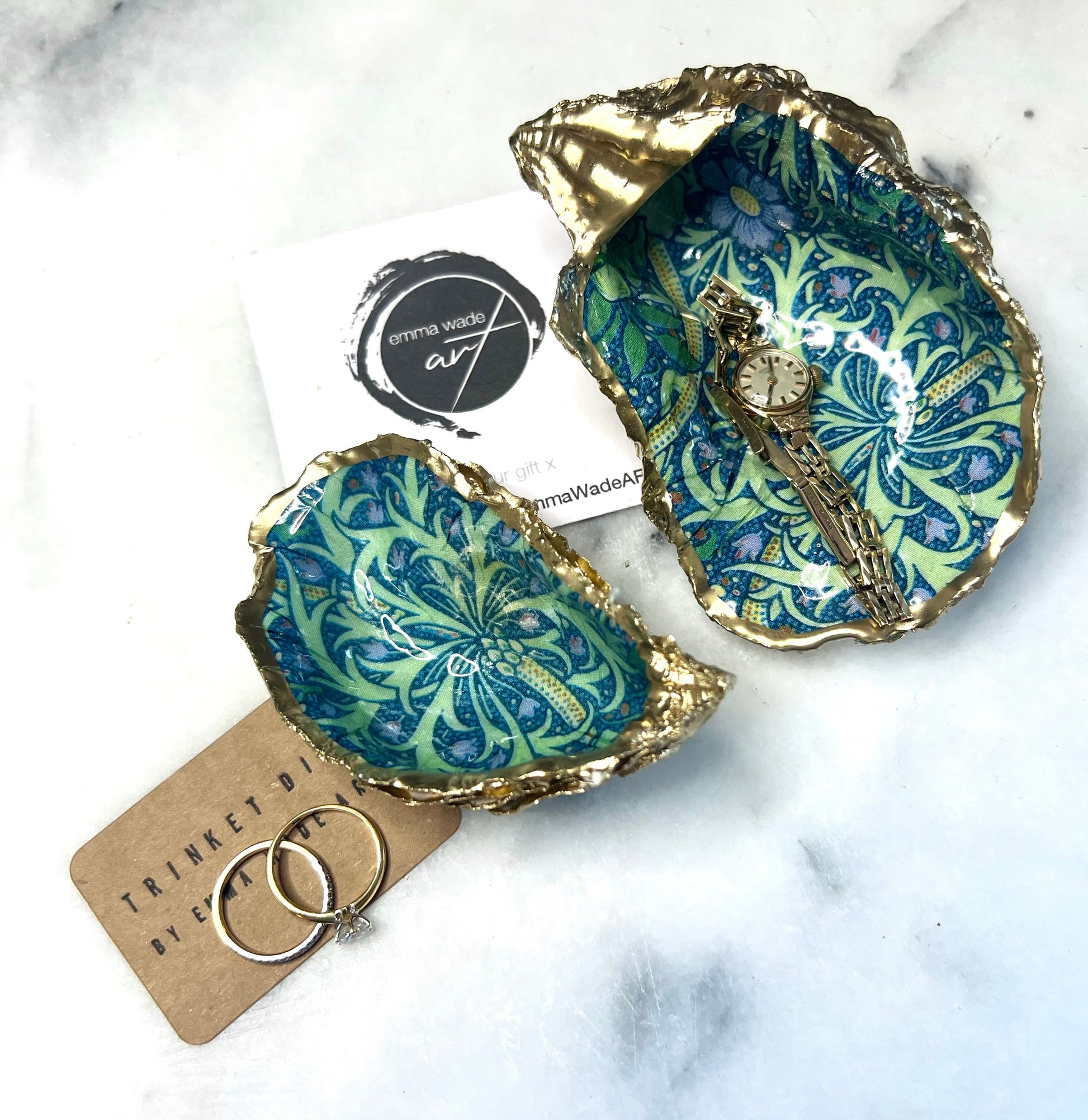 Handmade William Morris inspired oyster shell trinket dish in green and blue tones, finished with gold leaf and sealed with glossy resin. Coastal jewellery dish made from a Dorset oyster shell, featuring a seaweed decoupage design. Perfect for holding rings, earrings and small treasures. Decorative shell bowl photographed on a light background, showing the natural shell shape, detailed pattern and gilded edges.