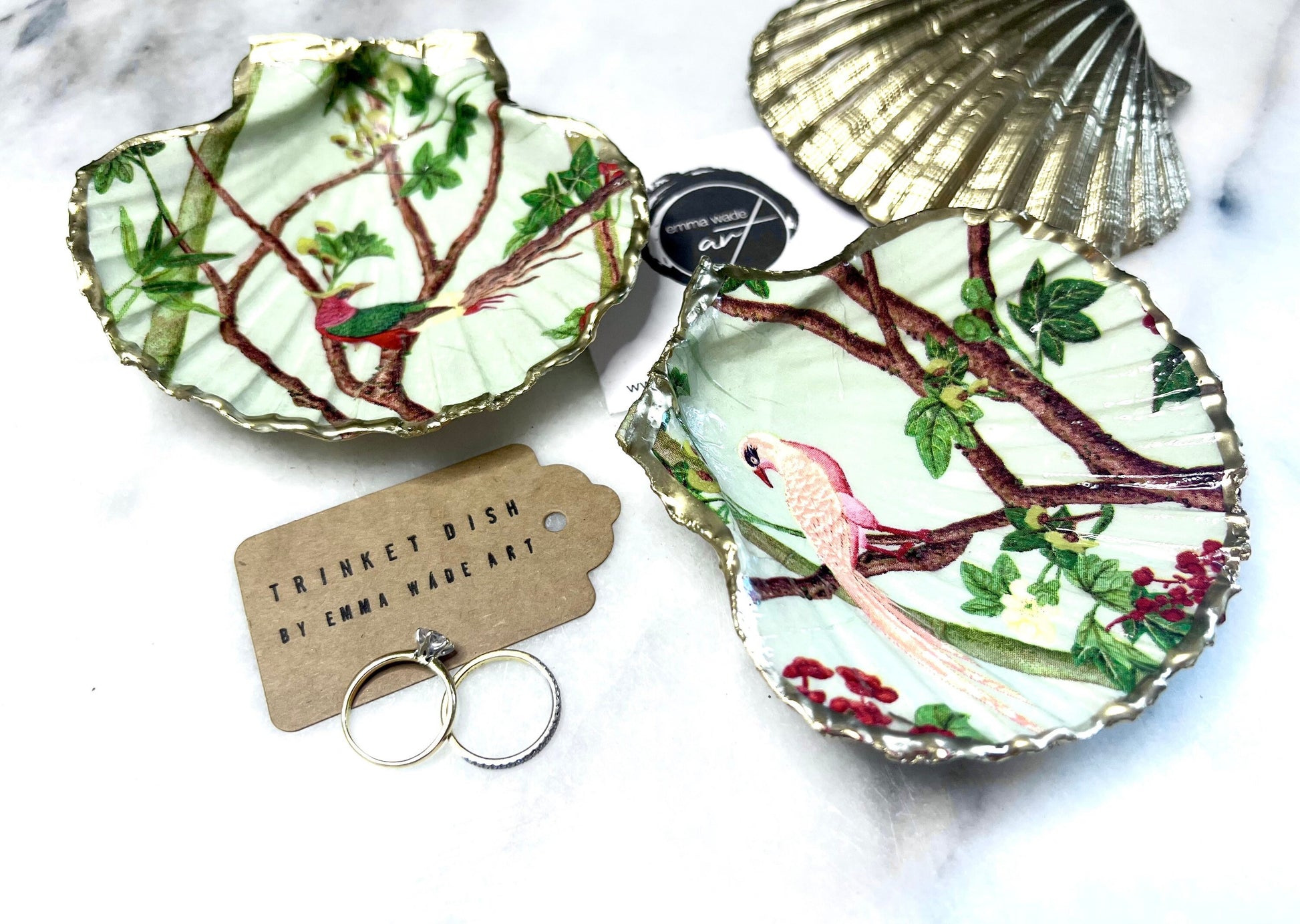 Handmade Dorset scallop shell trinket dish featuring delicate pink bird and botanical branch design with hand gilded gold leaf edging and glossy resin finish, elegant coastal jewellery holder inspired by birds of paradise and nature