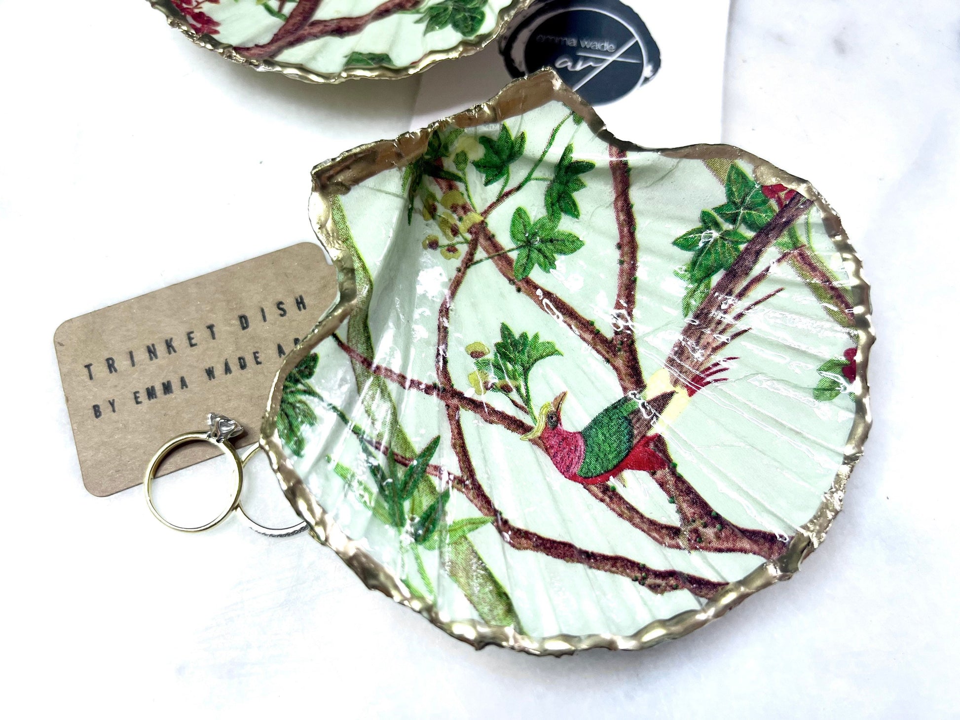 Handmade Dorset scallop shell trinket dish featuring delicate pink bird and botanical branch design with hand gilded gold leaf edging and glossy resin finish, elegant coastal jewellery holder inspired by birds of paradise and nature