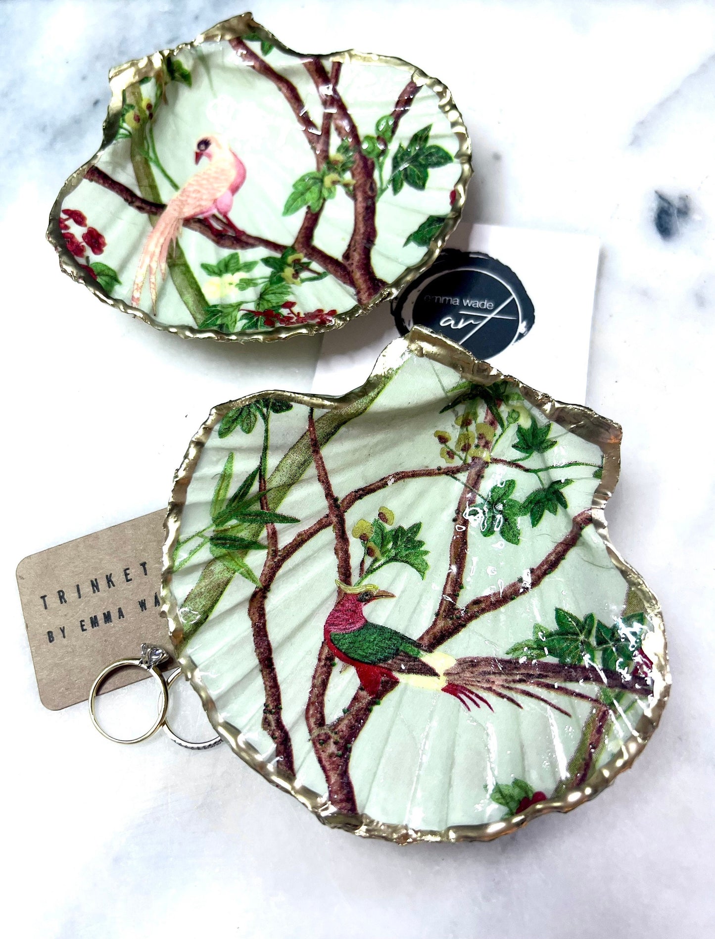 Handmade Dorset scallop shell trinket dish featuring delicate pink bird and botanical branch design with hand gilded gold leaf edging and glossy resin finish, elegant coastal jewellery holder inspired by birds of paradise and nature