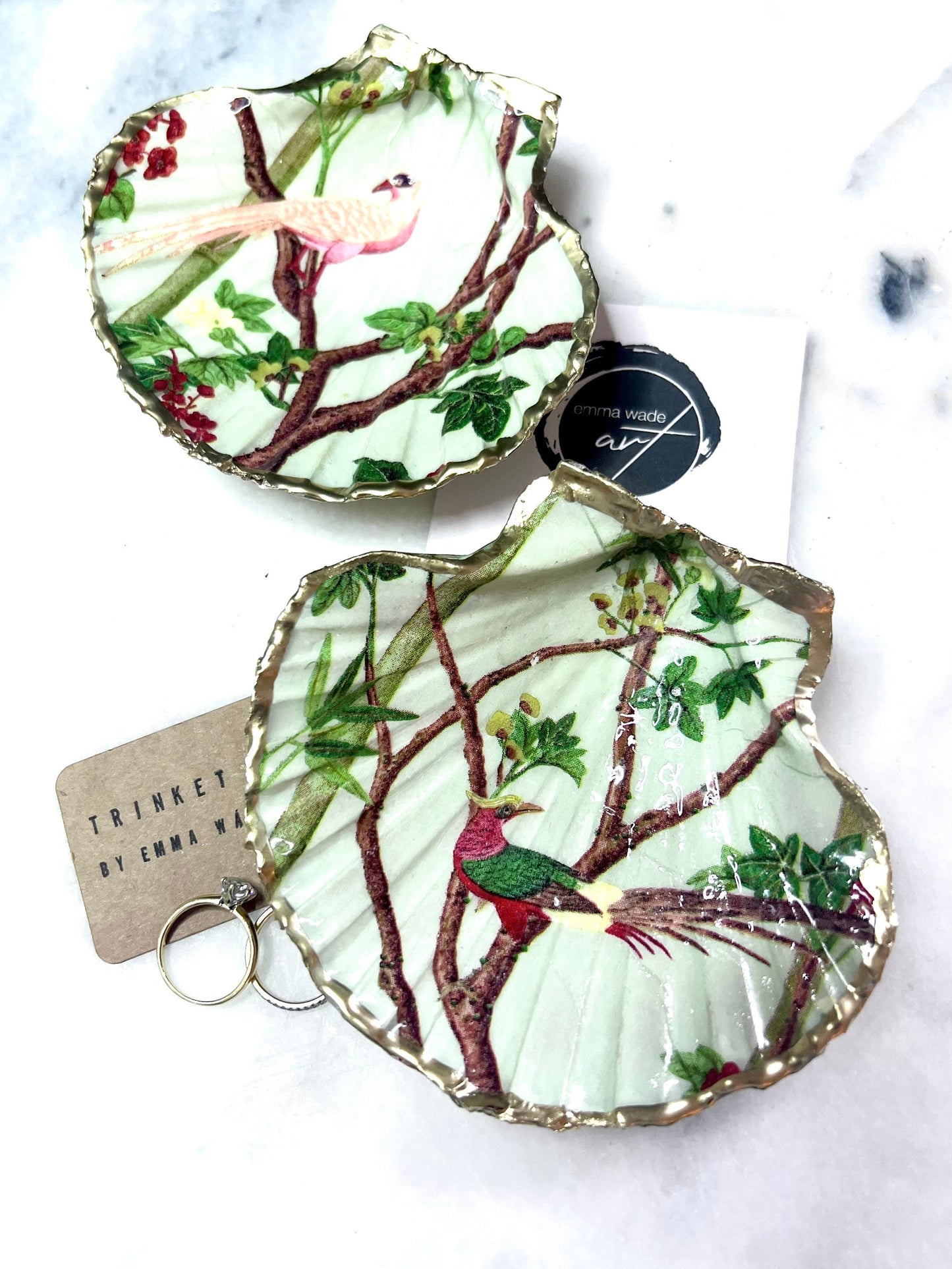 Handmade Dorset scallop shell trinket dish featuring delicate pink bird and botanical branch design with hand gilded gold leaf edging and glossy resin finish, elegant coastal jewellery holder inspired by birds of paradise and nature