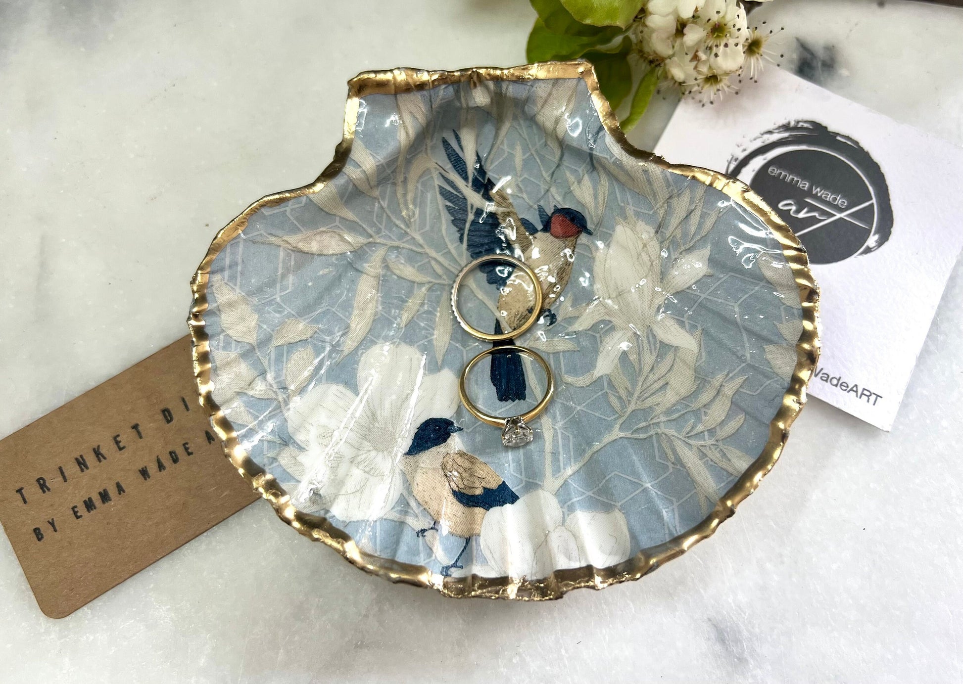 Handmade scallop shell trinket dish featuring a Blue Birds of Paradise decoupage design, finished with real gold leaf and sealed with glossy resin. Crafted from a natural Dorset scallop shell and shown as a jewellery and ring holder on a light background. Coastal-inspired home decor, perfect for holding rings, earrings and small keepsakes, with each shell one of a kind and finished by hand.