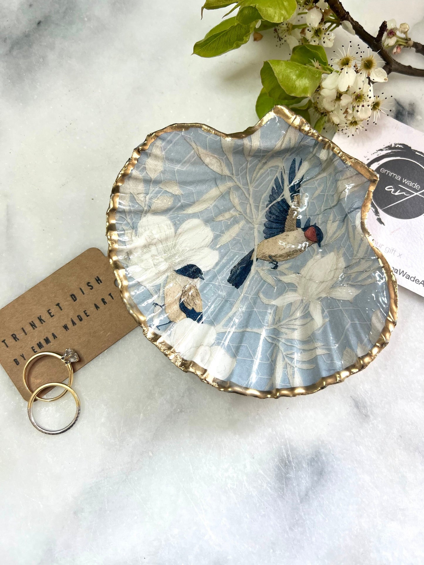 Handmade scallop shell trinket dish featuring a Blue Birds of Paradise decoupage design, finished with real gold leaf and sealed with glossy resin. Crafted from a natural Dorset scallop shell and shown as a jewellery and ring holder on a light background. Coastal-inspired home decor, perfect for holding rings, earrings and small keepsakes, with each shell one of a kind and finished by hand.
