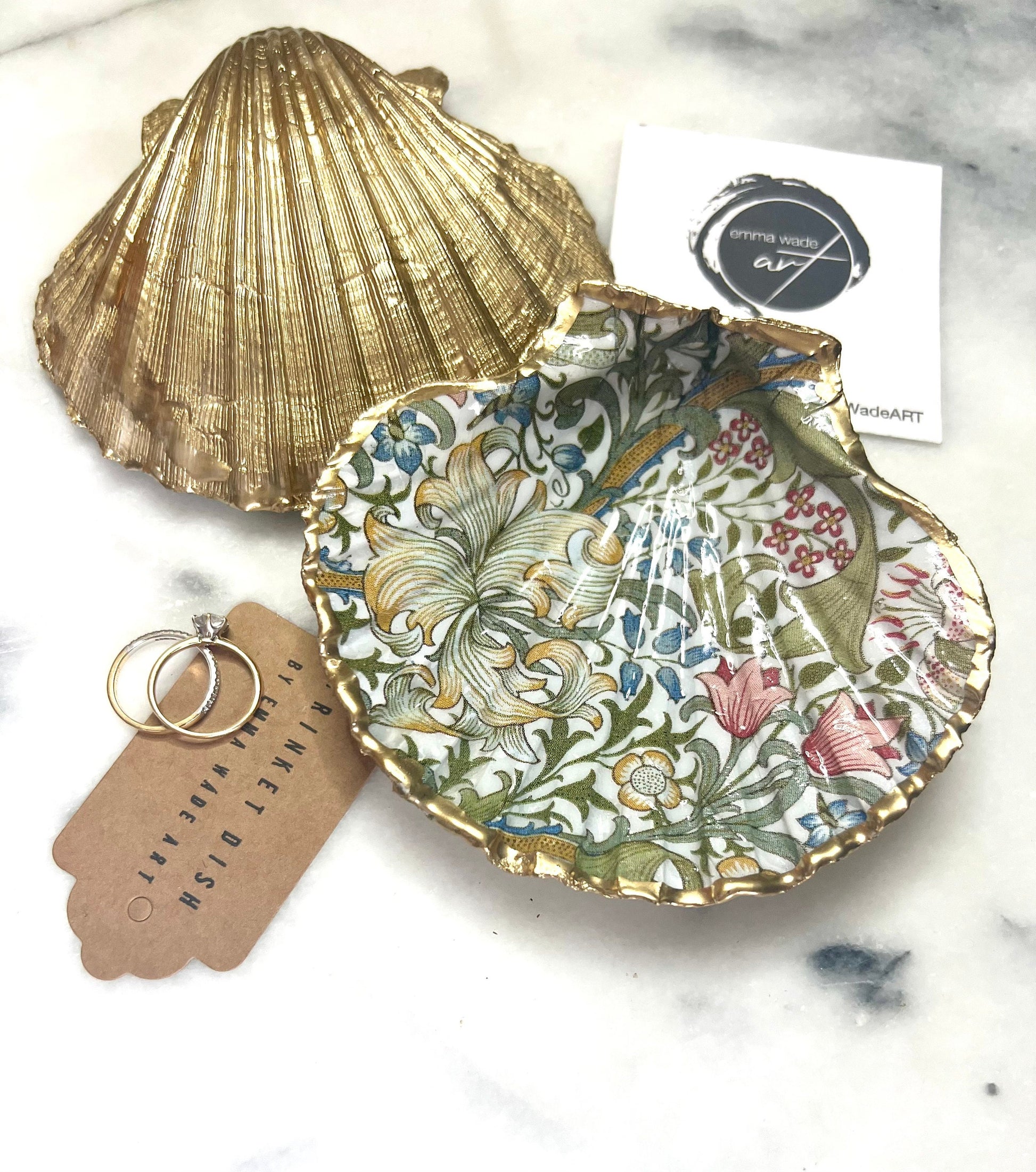 Handcrafted Dorset scallop shell trinket dish featuring William Morris Golden Lily floral design. Natural shell edged with hand applied gold leaf and sealed with glossy resin. Heritage floral jewellery holder displayed with rings on marble surface. Elegant coastal home decor gift.