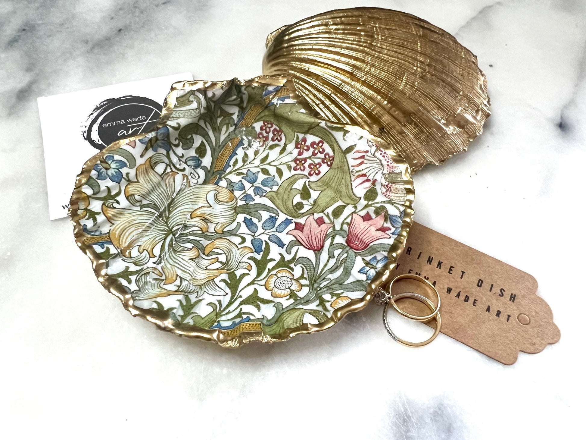 Handcrafted Dorset scallop shell trinket dish featuring William Morris Golden Lily floral design. Natural shell edged with hand applied gold leaf and sealed with glossy resin. Heritage floral jewellery holder displayed with rings on marble surface. Elegant coastal home decor gift.