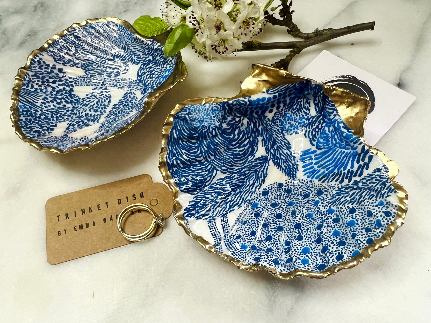 Marimekko inspired blue floral scallop shell trinket dish with hand-applied gold leaf edging and glossy resin finish. Natural Dorset shell jewellery holder featuring bold Scandinavian style botanical pattern. Decorative coastal ring dish styled on a marble surface, ideal as a bedside trinket bowl, host gift or luxury handmade home accent.
