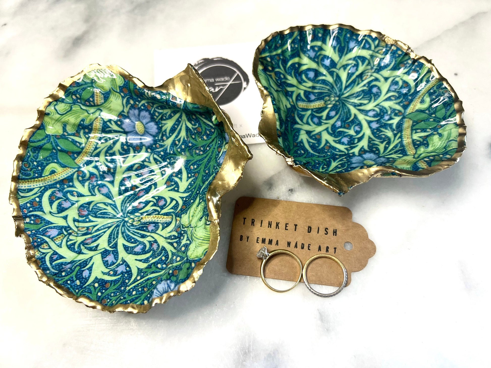 Handmade William Morris inspired scallop shell trinket dish in green and blue tones, featuring a seaweed decoupage design. Finished with gold leaf and sealed with glossy resin. Coastal jewellery dish made from a UK scallop shell, perfect for holding rings, earrings and small treasures. Decorative shell bowl photographed on a light background, showing the natural shell shape and gilded edges.