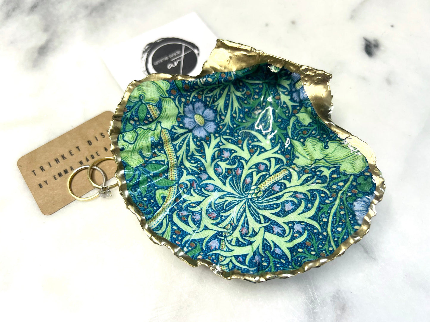 Handmade William Morris inspired scallop shell trinket dish in green and blue tones, featuring a seaweed decoupage design. Finished with gold leaf and sealed with glossy resin. Coastal jewellery dish made from a UK scallop shell, perfect for holding rings, earrings and small treasures. Decorative shell bowl photographed on a light background, showing the natural shell shape and gilded edges.