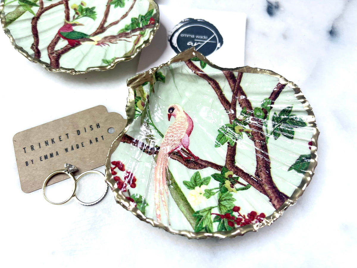 Handmade Dorset scallop shell trinket dish featuring delicate pink bird and botanical branch design with hand gilded gold leaf edging and glossy resin finish, elegant coastal jewellery holder inspired by birds of paradise and nature