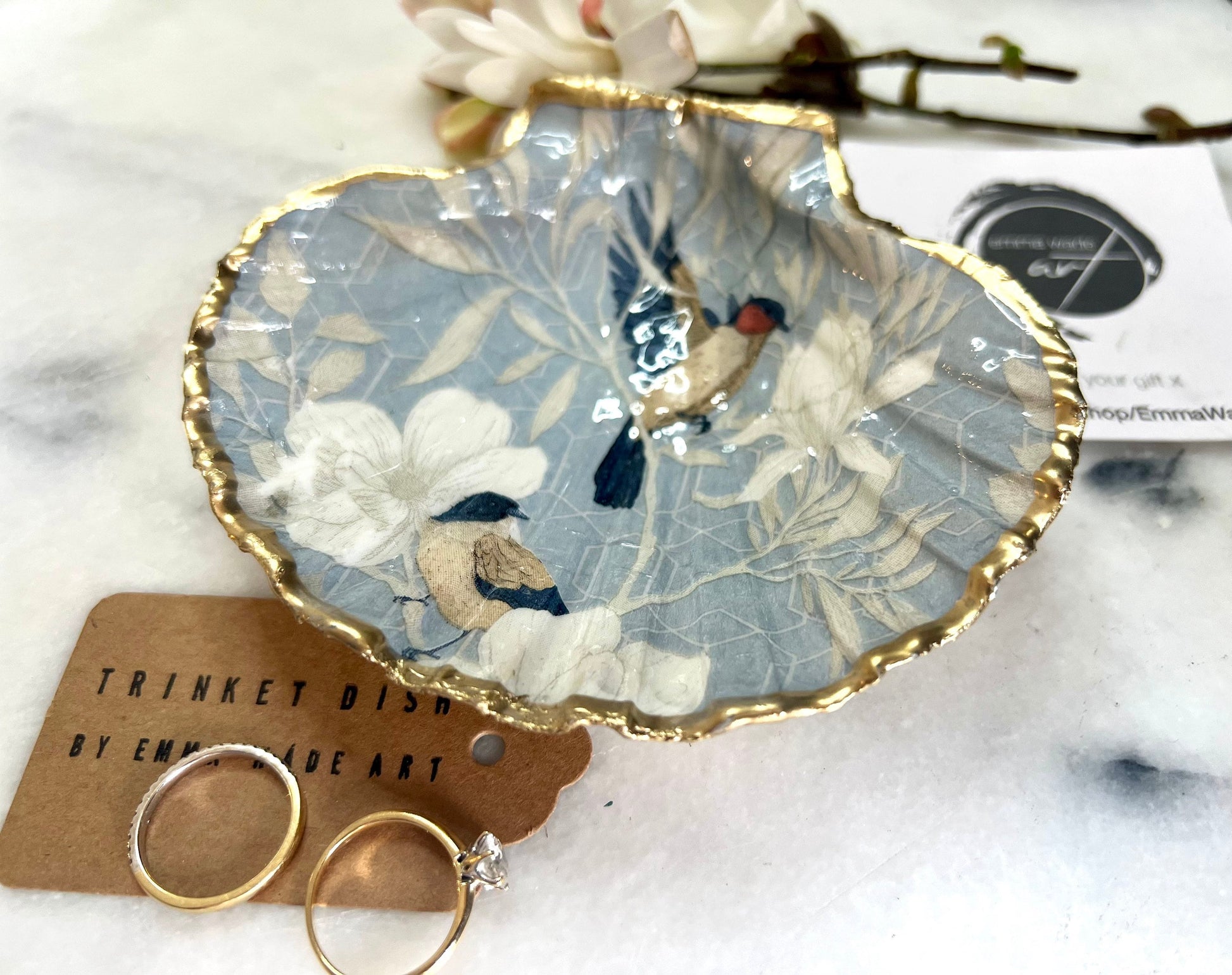 Handmade scallop shell trinket dish featuring a Blue Birds of Paradise decoupage design, finished with real gold leaf and sealed with glossy resin. Crafted from a natural Dorset scallop shell and shown as a jewellery and ring holder on a light background. Coastal-inspired home decor, perfect for holding rings, earrings and small keepsakes, with each shell one of a kind and finished by hand.