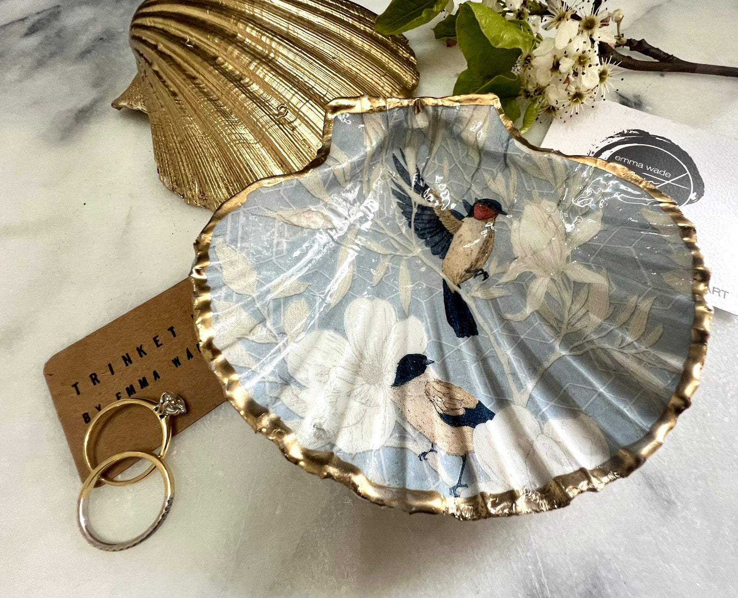 Handmade scallop shell trinket dish featuring a Blue Birds of Paradise decoupage design, finished with real gold leaf and sealed with glossy resin. Crafted from a natural Dorset scallop shell and shown as a jewellery and ring holder on a light background. Coastal-inspired home decor, perfect for holding rings, earrings and small keepsakes, with each shell one of a kind and finished by hand.