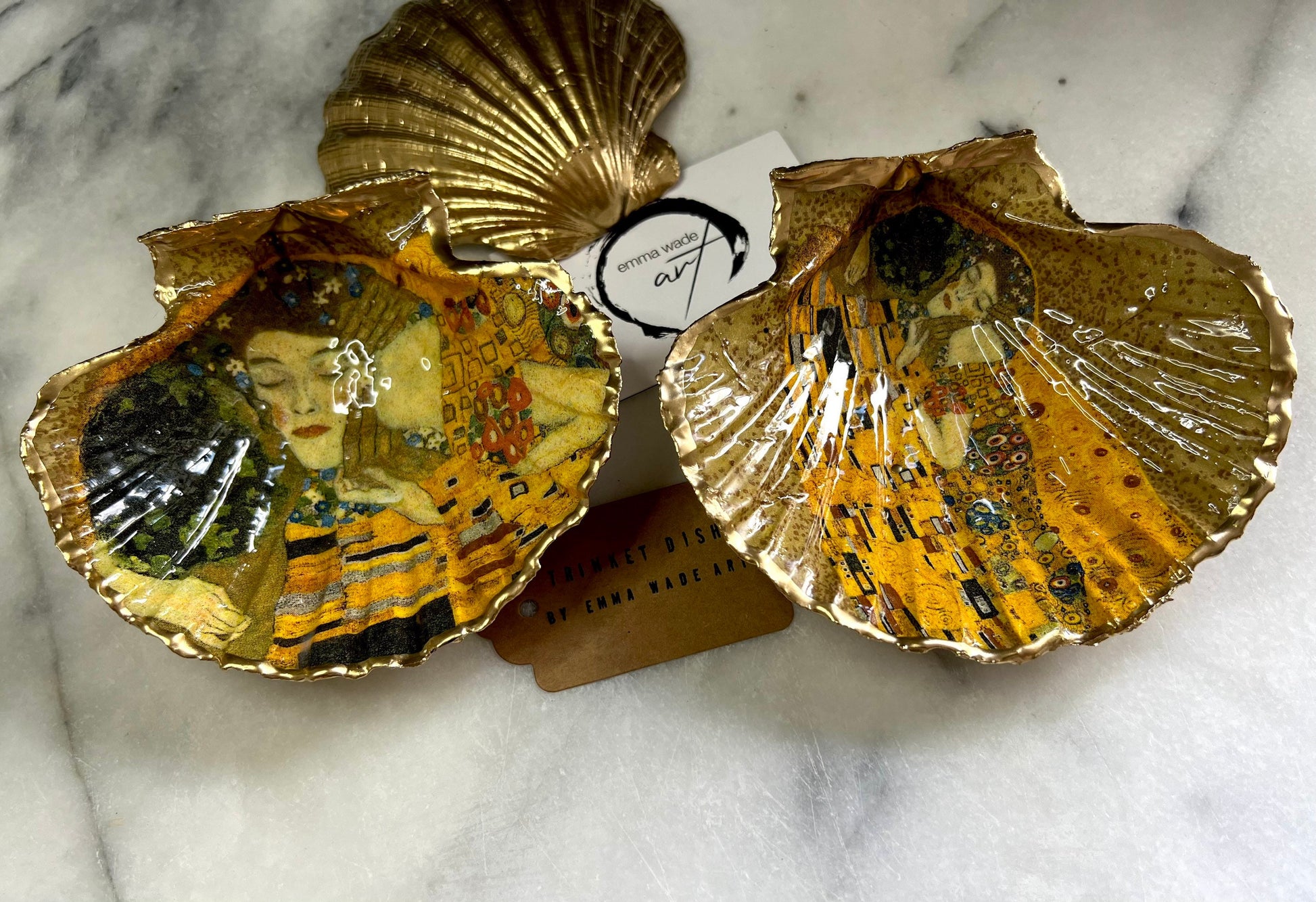 Handmade scallop shell trinket dish inspired by Gustav Klimt’s “The Kiss”, finished with gold leaf and sealed with glossy resin. Coastal Dorset shell jewellery dish perfect for rings, earrings and small treasures. Unique decorative shell bowl with golden artwork design, photographed on a light background showing detailed gilded surface and natural shell shape.