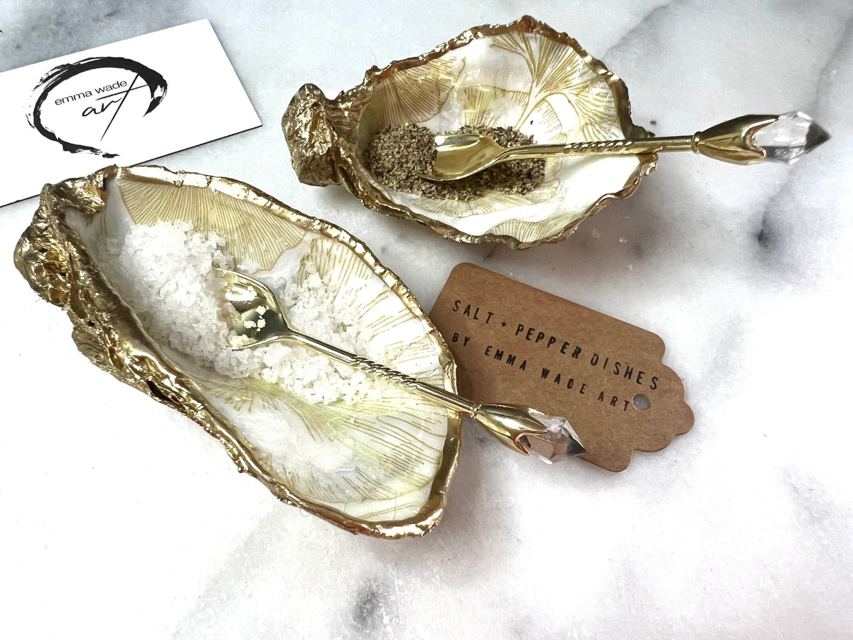 Pair of handmade Dorset oyster shell salt and pepper pinch pots featuring elegant Japanese Ginkgo floral artwork in soft gold and pearl tones with hand-applied gold leaf edging. Coastal luxury cruet set sealed in glossy Crystal resin with optional gold crystal spoons.