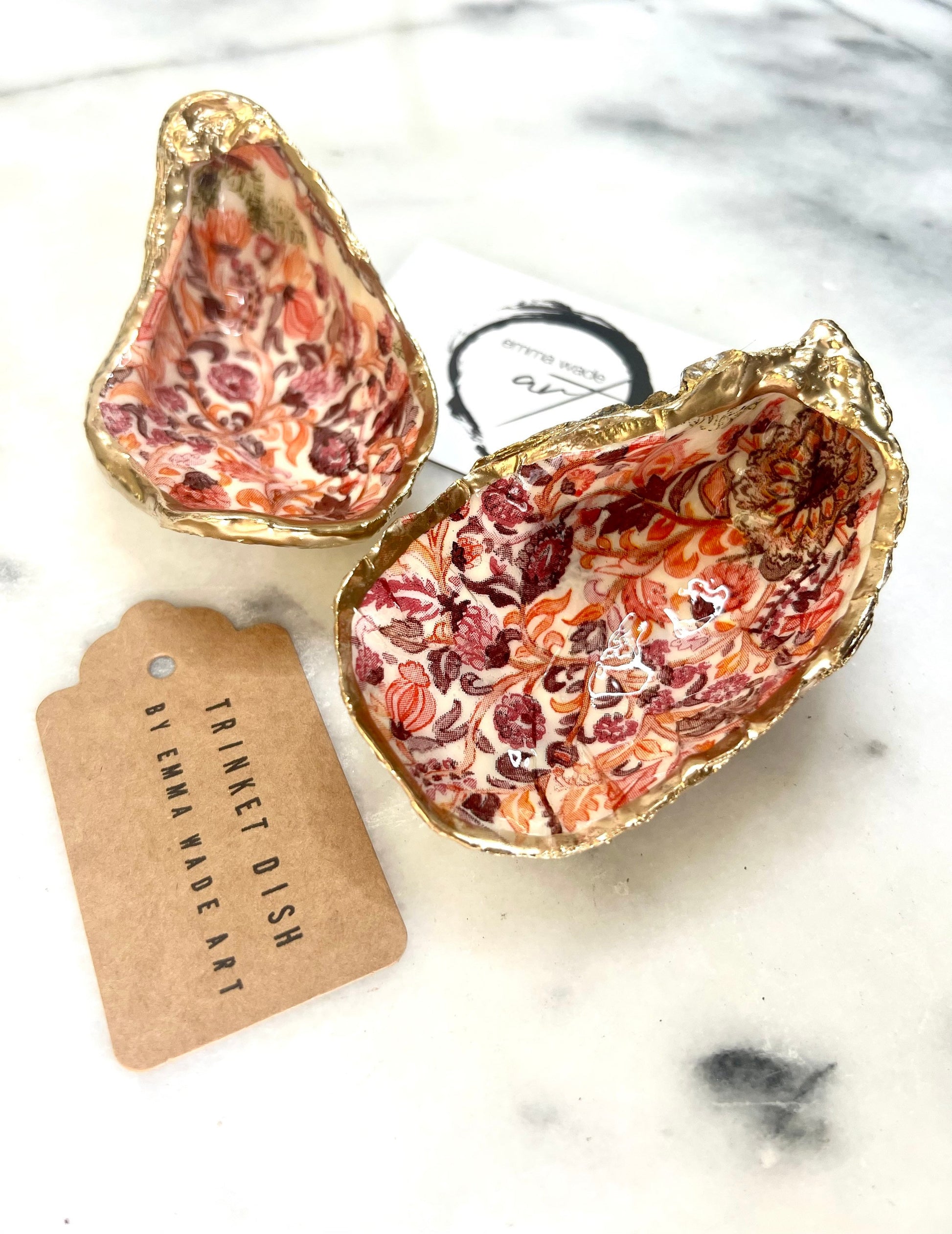 Handmade Dorset oyster shell trinket dishes featuring a William Morris style pink coral floral botanical pattern with luxurious liquid gold leaf edging. Natural oyster shells are sealed in glossy crystal clear resin and styled as heritage jewellery holders, vanity trays and coastal home décor accessories. Elegant vintage floral shell dishes photographed on a marble background with decorative styling.