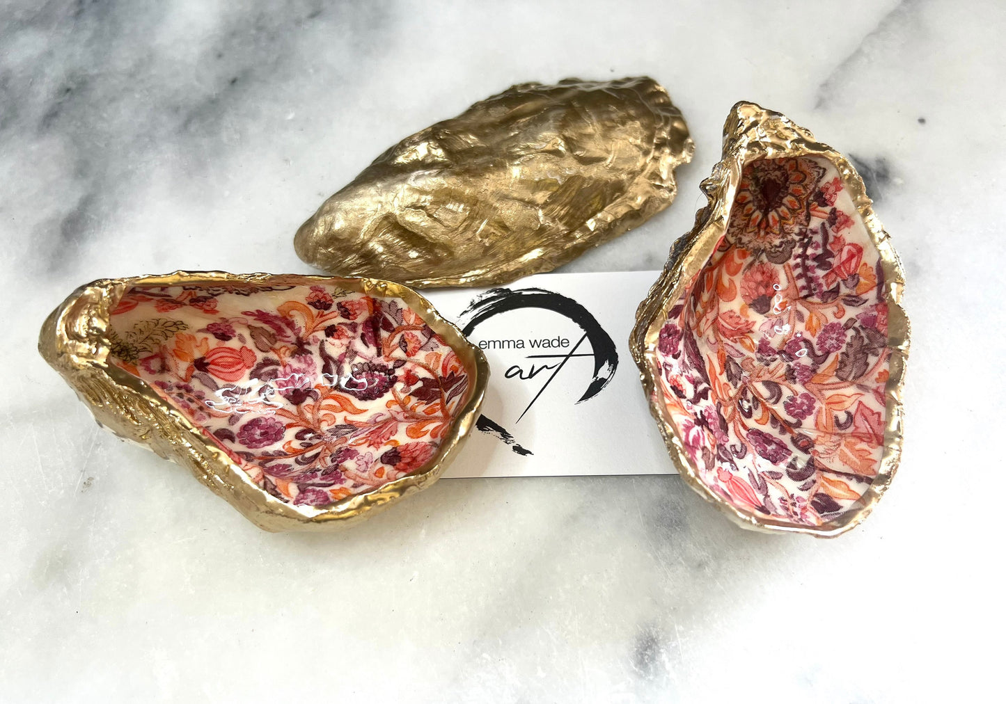 Handmade Dorset oyster shell trinket dishes featuring a William Morris style pink coral floral botanical pattern with luxurious liquid gold leaf edging. Natural oyster shells are sealed in glossy crystal clear resin and styled as heritage jewellery holders, vanity trays and coastal home décor accessories. Elegant vintage floral shell dishes photographed on a marble background with decorative styling.