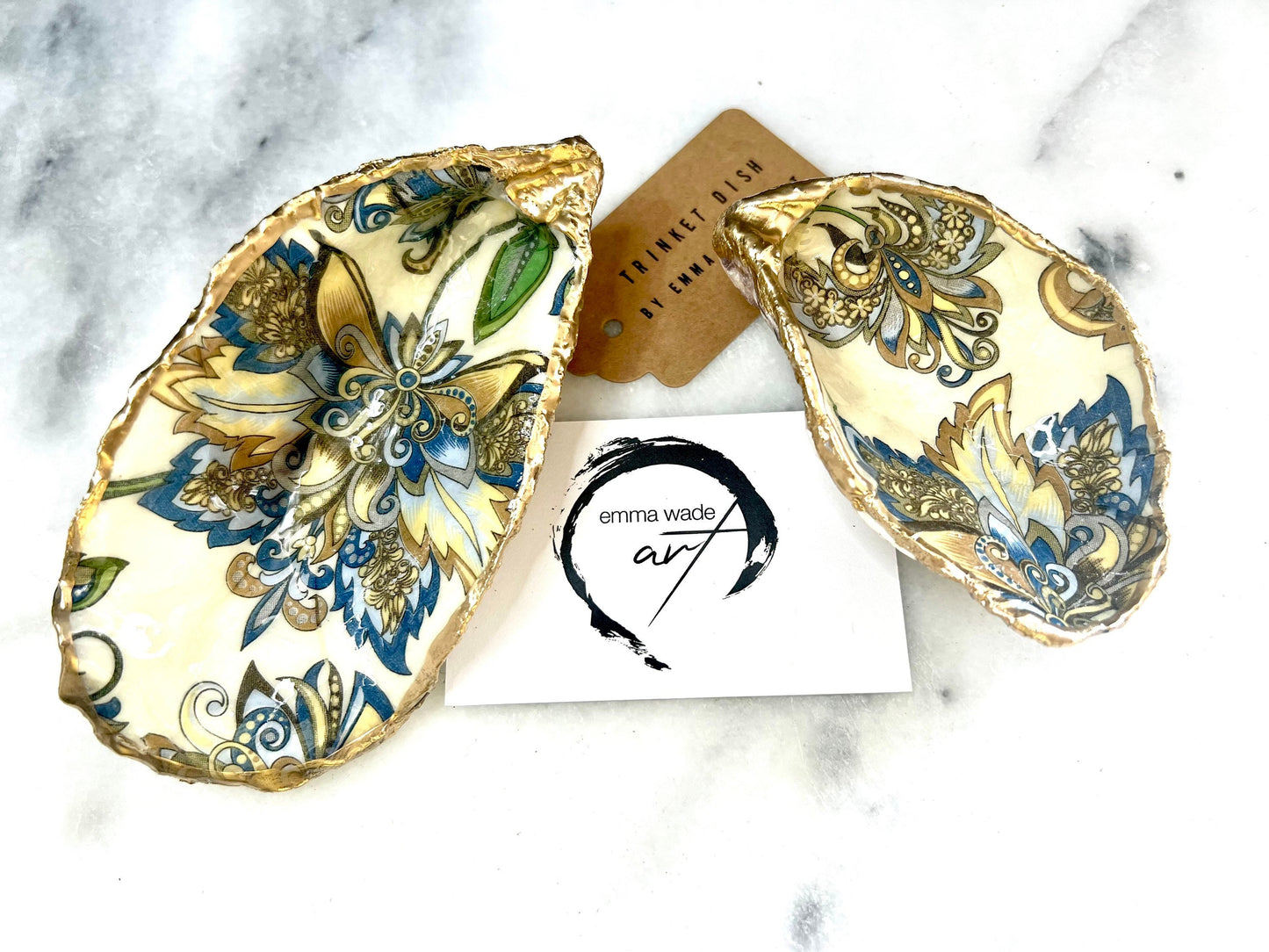 Handmade Dorset oyster shell trinket dishes decorated with ornate blue, green and gold baroque floral patterns inspired by antique European porcelain and vintage decorative art. Natural oyster shells are hand gilded with liquid gold leaf edging and sealed with glossy crystal clear resin. Luxury coastal jewelry holders and vanity dishes photographed on marble background with elegant decorative styling.