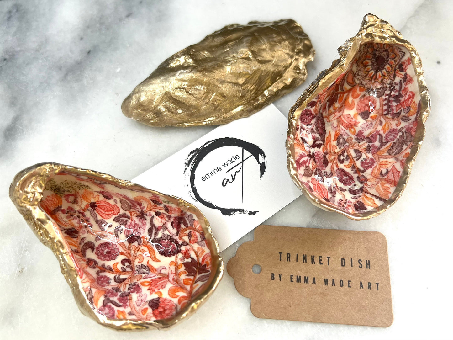 Handmade Dorset oyster shell trinket dishes featuring a William Morris style pink coral floral botanical pattern with luxurious liquid gold leaf edging. Natural oyster shells are sealed in glossy crystal clear resin and styled as heritage jewellery holders, vanity trays and coastal home décor accessories. Elegant vintage floral shell dishes photographed on a marble background with decorative styling.