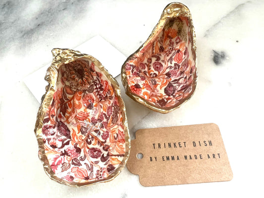 Handmade Dorset oyster shell trinket dishes featuring a William Morris style pink coral floral botanical pattern with luxurious liquid gold leaf edging. Natural oyster shells are sealed in glossy crystal clear resin and styled as heritage jewellery holders, vanity trays and coastal home décor accessories. Elegant vintage floral shell dishes photographed on a marble background with decorative styling.