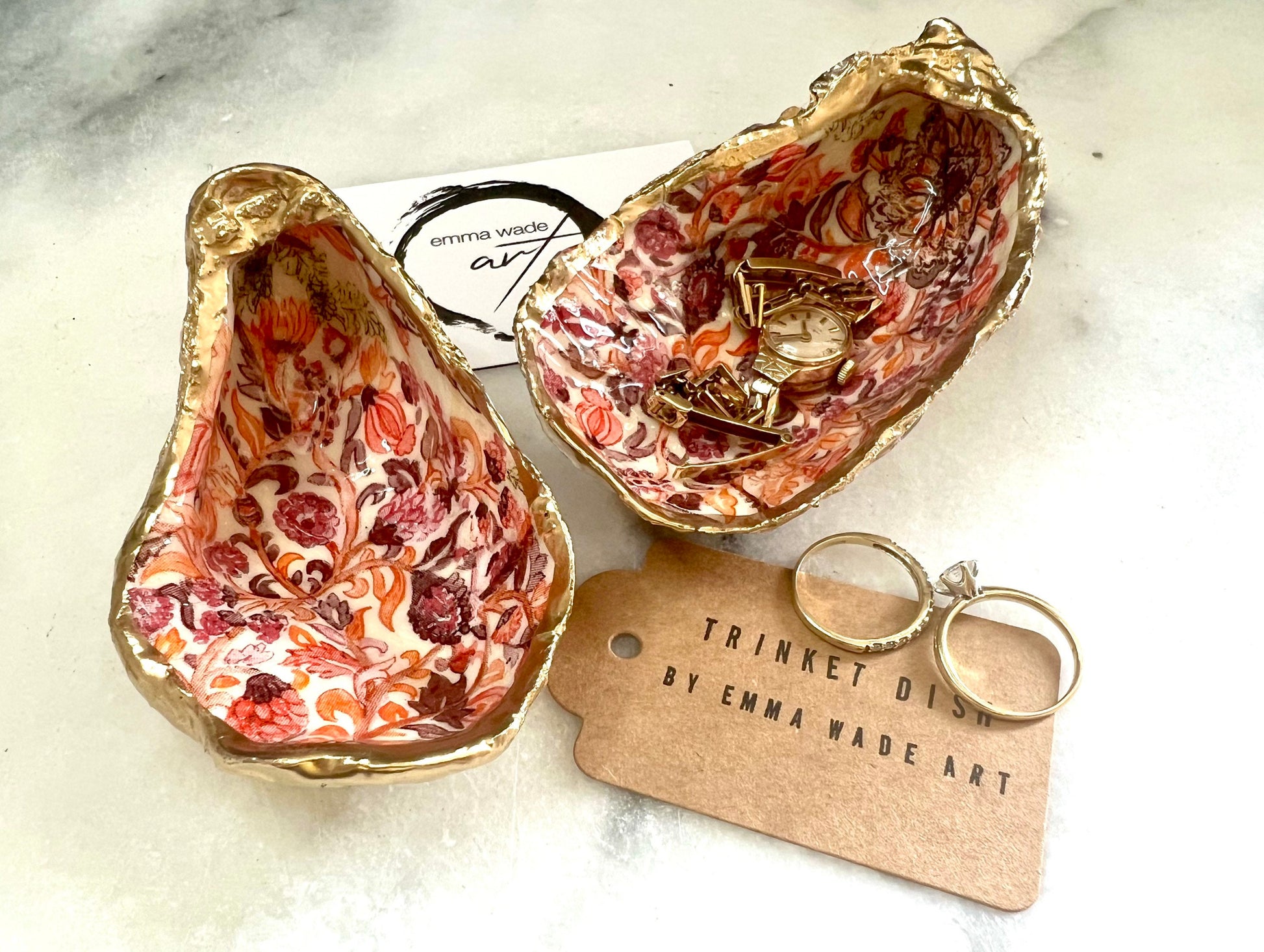 Handmade Dorset oyster shell trinket dishes featuring a William Morris style pink coral floral botanical pattern with luxurious liquid gold leaf edging. Natural oyster shells are sealed in glossy crystal clear resin and styled as heritage jewellery holders, vanity trays and coastal home décor accessories. Elegant vintage floral shell dishes photographed on a marble background with decorative styling.