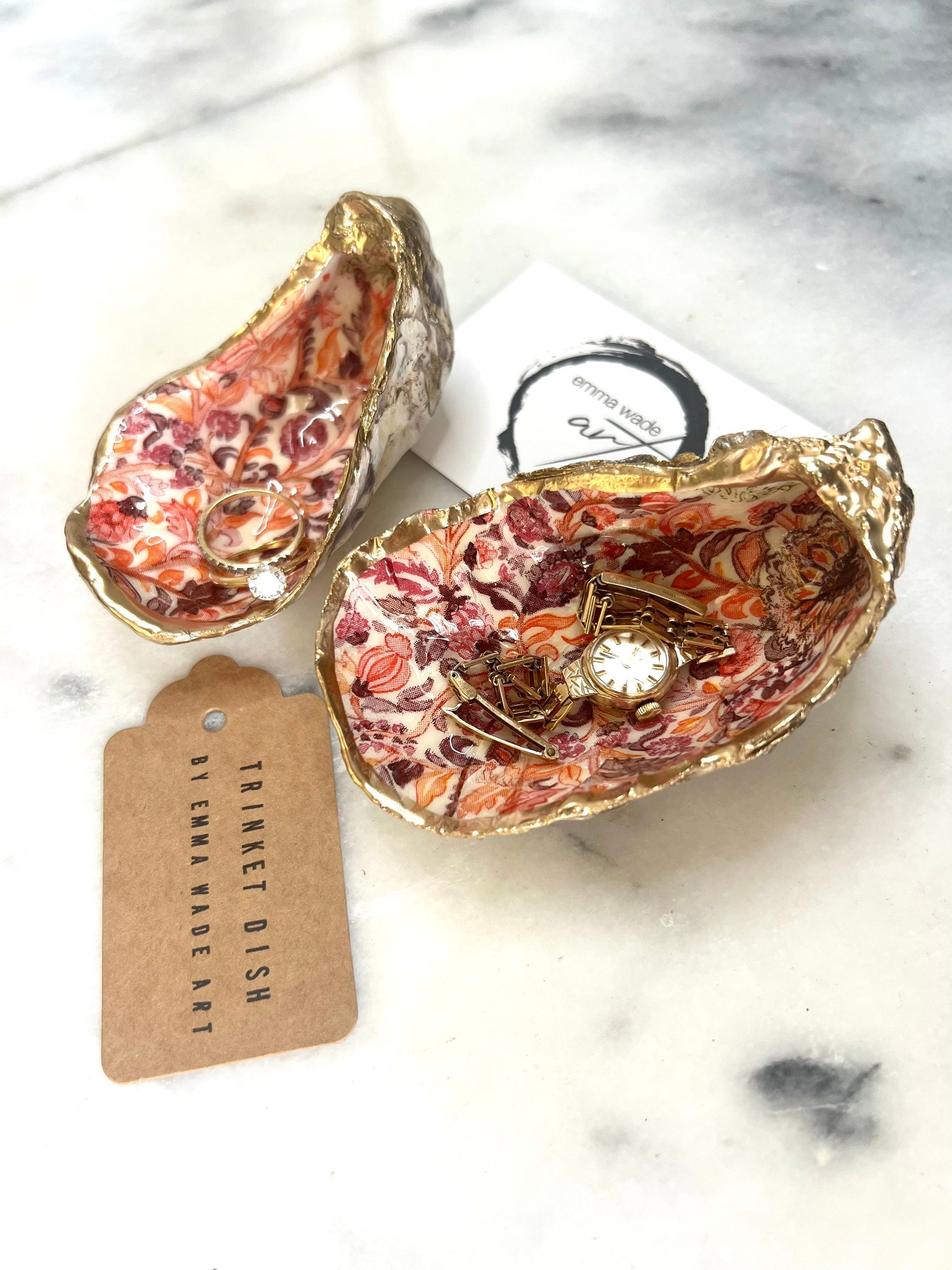 Handmade Dorset oyster shell trinket dishes featuring a William Morris style pink coral floral botanical pattern with luxurious liquid gold leaf edging. Natural oyster shells are sealed in glossy crystal clear resin and styled as heritage jewellery holders, vanity trays and coastal home décor accessories. Elegant vintage floral shell dishes photographed on a marble background with decorative styling.