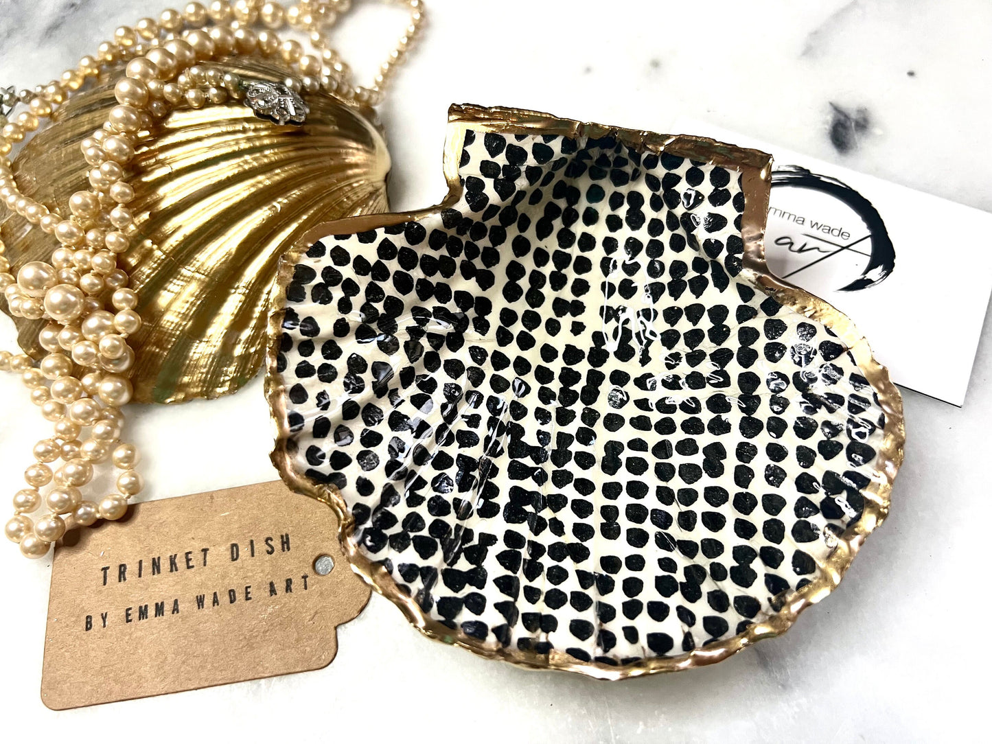 Handcrafted black and white dotted Dorset scallop shell trinket dish, gilded with real gold leaf and sealed in crystal-clear resin. Perfect as a jewellery holder, cufflink tray, tea light holder, or coastal home accent. Each eco-friendly shell is ethically sourced from the Dorset coastline, individually hand finished in Surrey, and presented in a sustainable gift box. A thoughtful handmade gift for ocean lovers, weddings, birthdays, or coastal home décor.